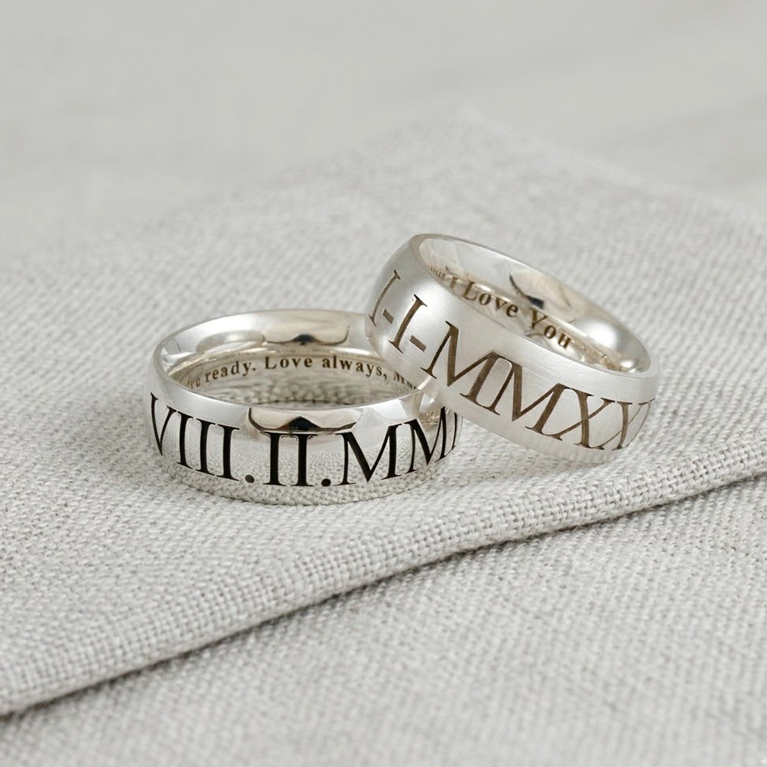 Two silver rings with Roman numeral inscriptions on a textured gray surface