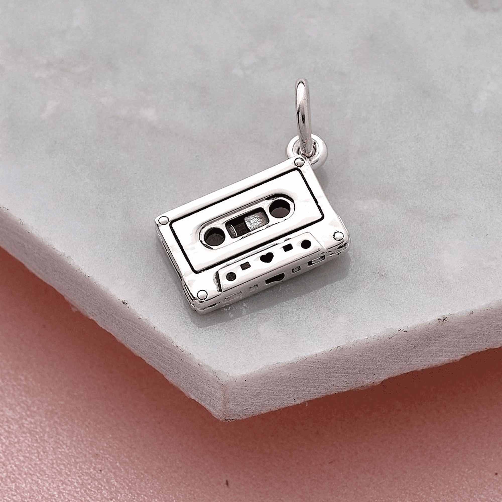 Silver cassette tape charm on a light gray surface
