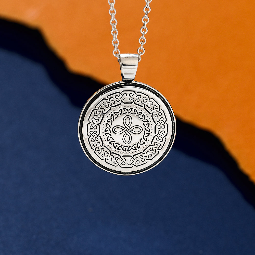 Silver necklace with a round pendant featuring intricate celtic knot patterns on an orange and blue gradient background.
