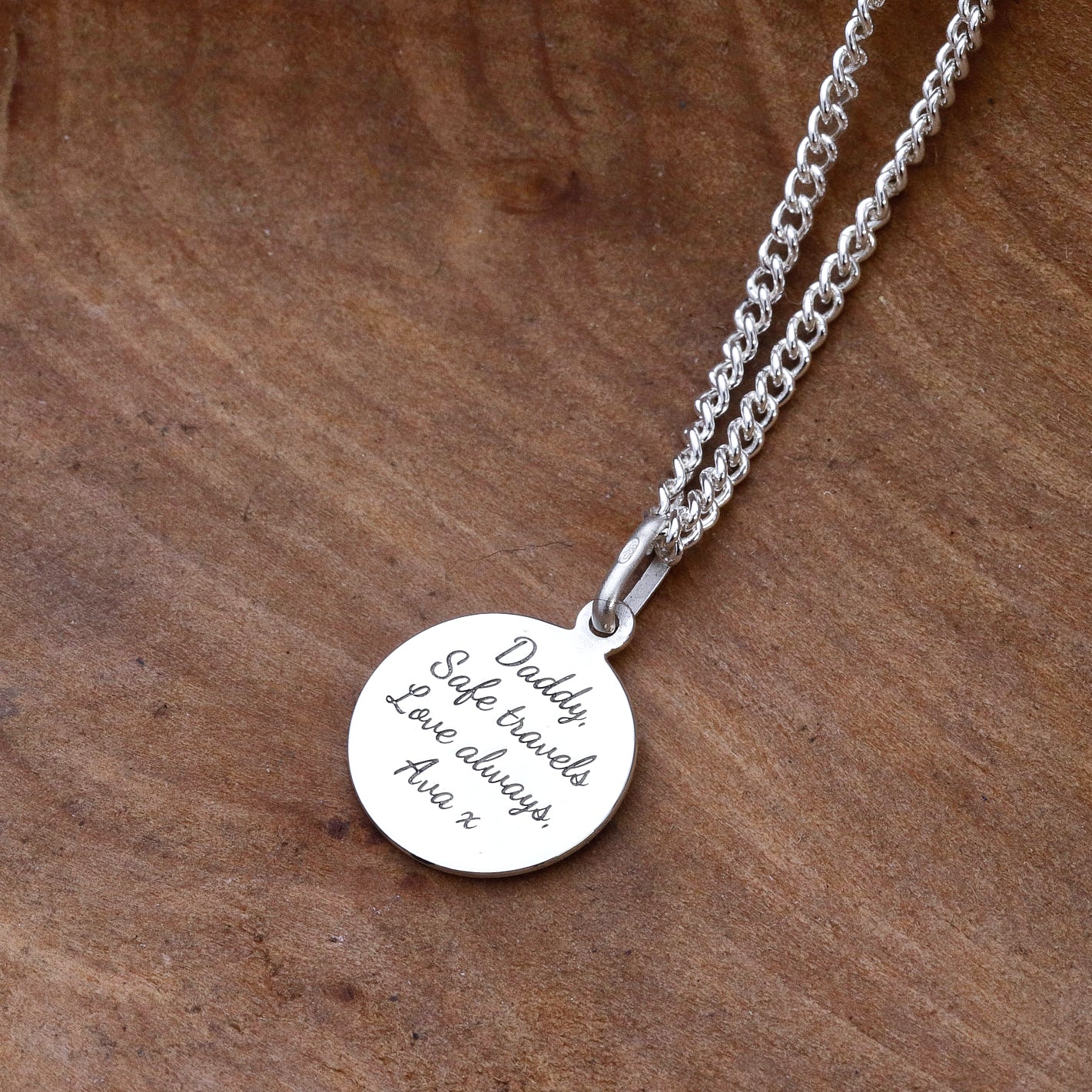 Silver necklace with a engraved pendant on a wooden surface