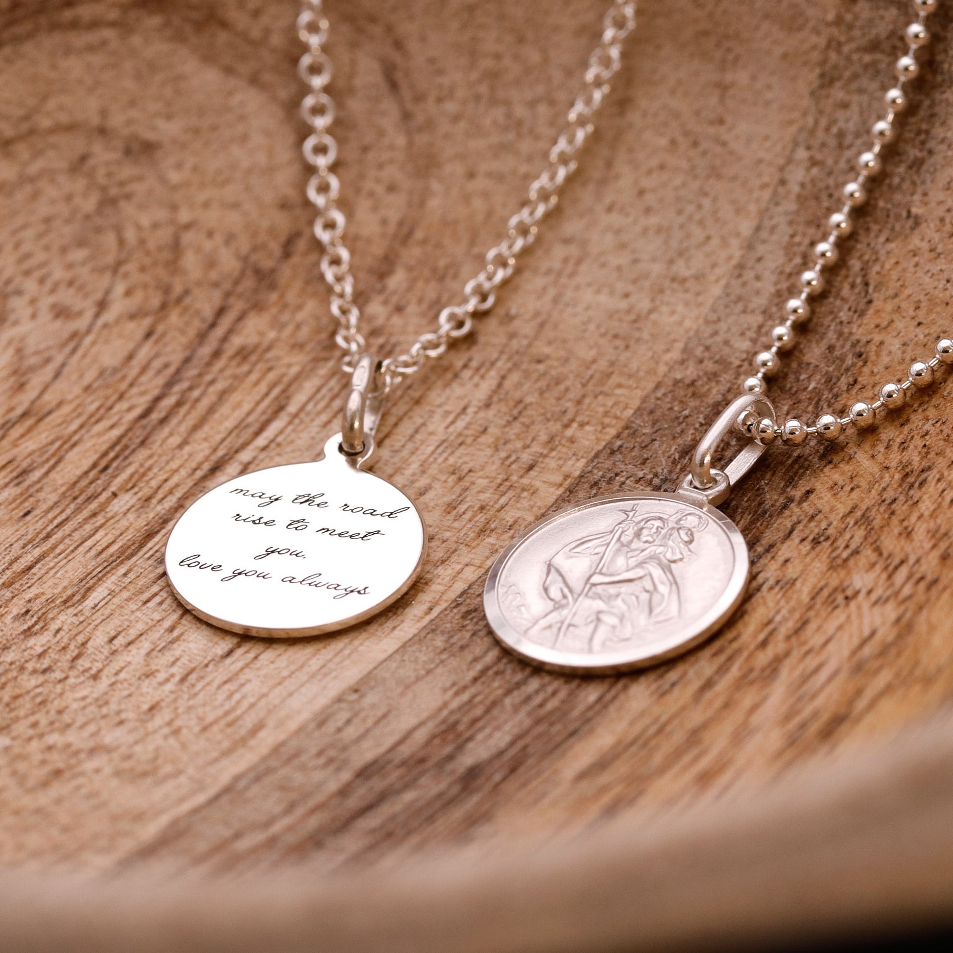 Two silver necklaces with engraved pendants on a wooden surface