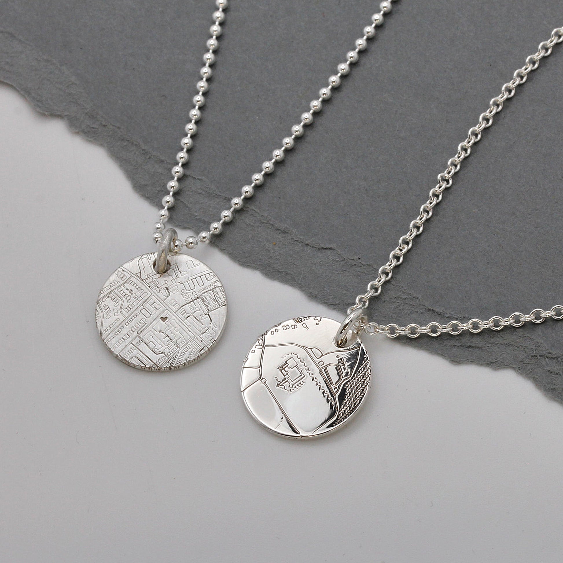 Two silver necklaces with textured pendants on a gray surface