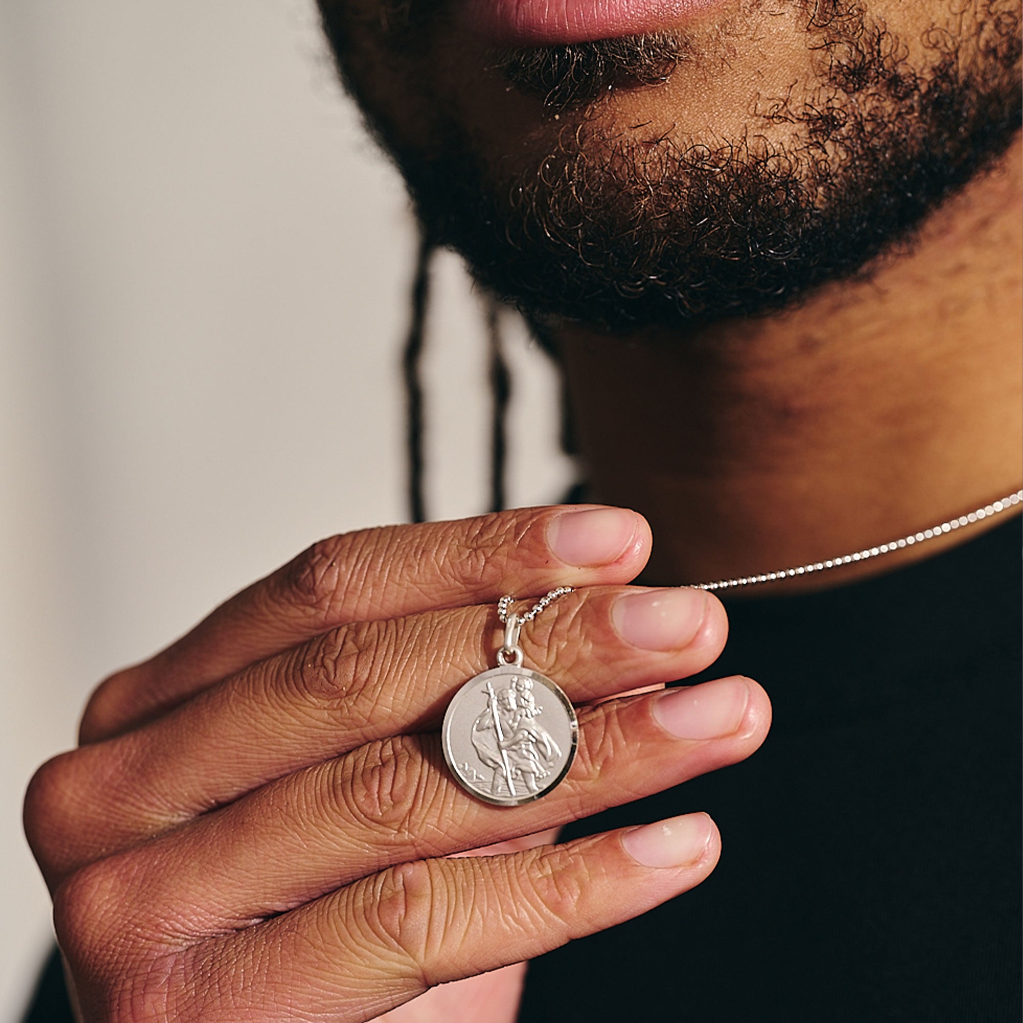 Person holding a silver necklace with a round pendant