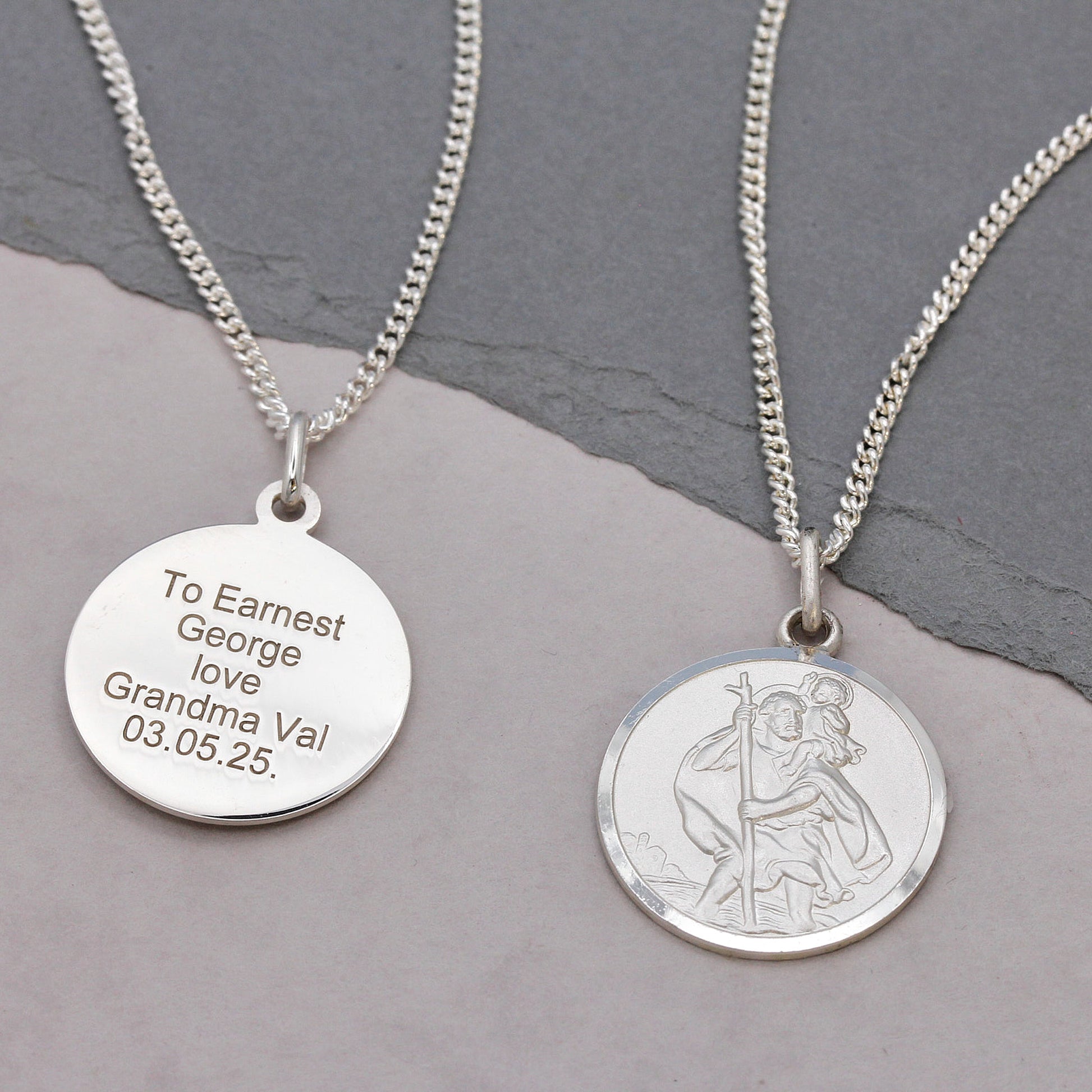 Two silver necklaces with engraved messages on a gray surface