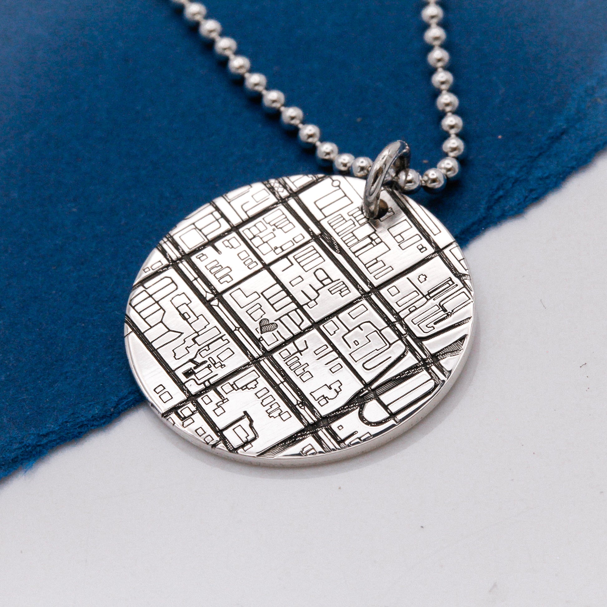 Silver necklace with a round pendant featuring a detailed map design on a blue and white background.