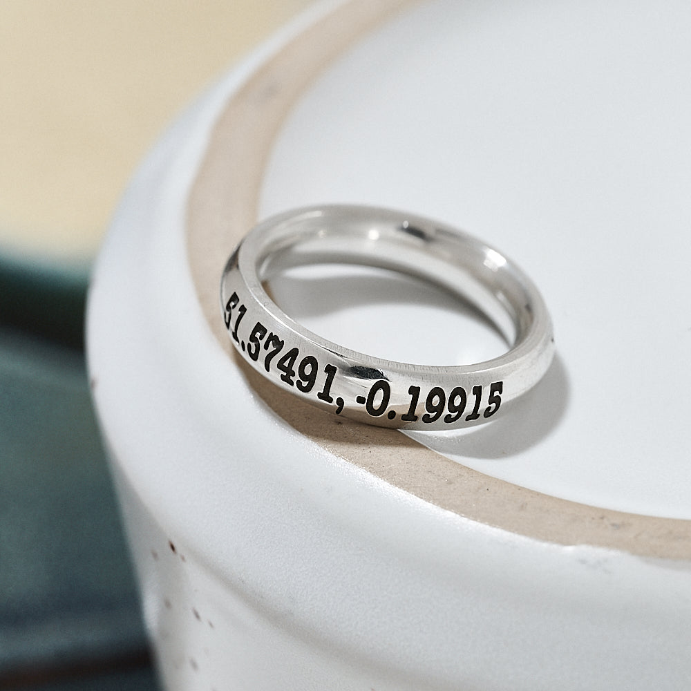 Silver ring with engraved latitude longitude coordinates on a white surface