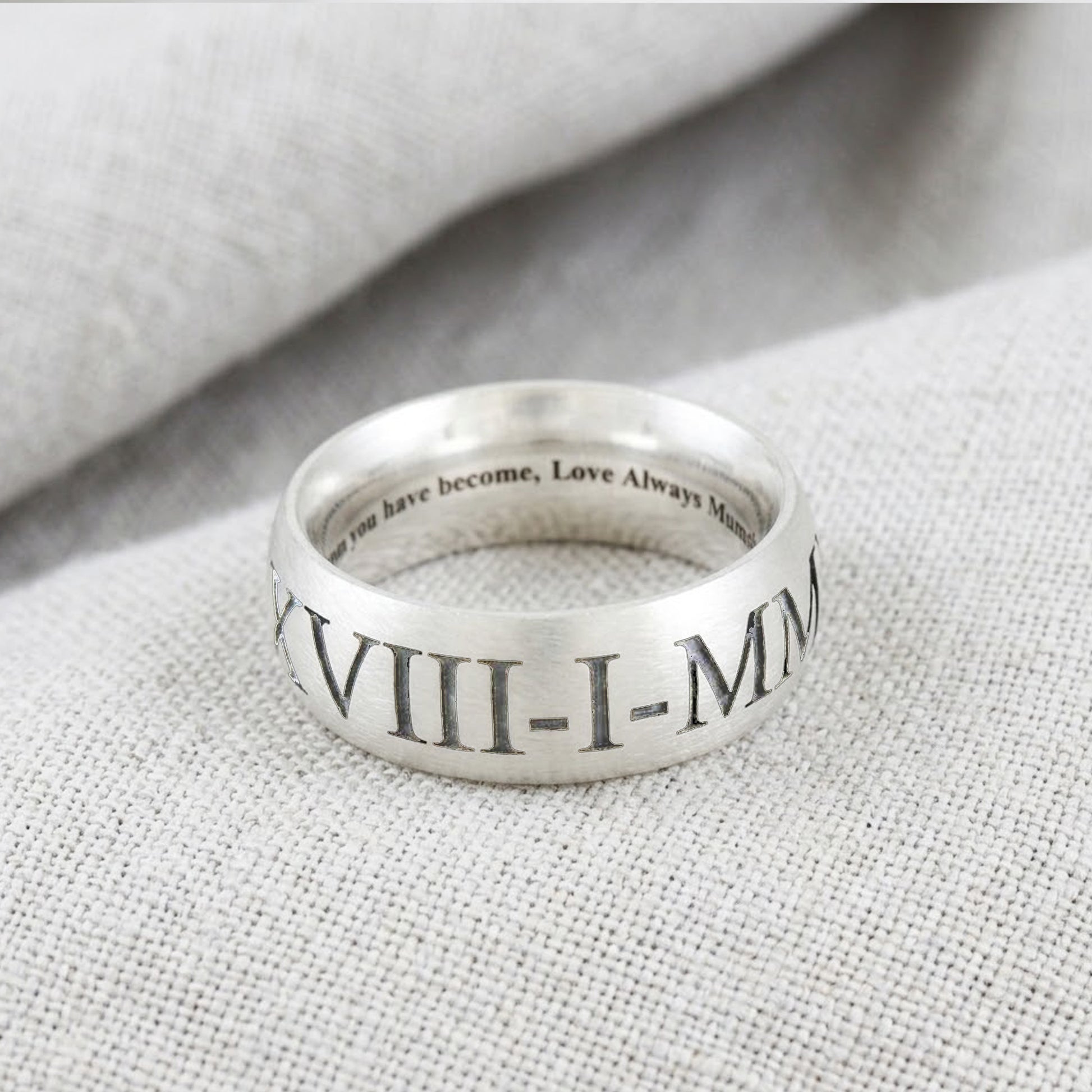 Silver ring with Roman numerals and engraved text on a textured fabric background