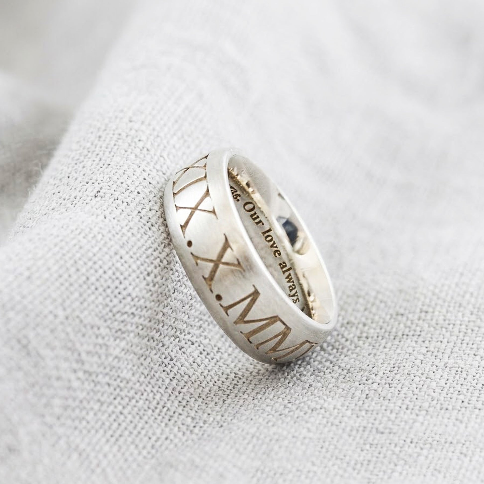 Silver ring with engraved text on a textured fabric background