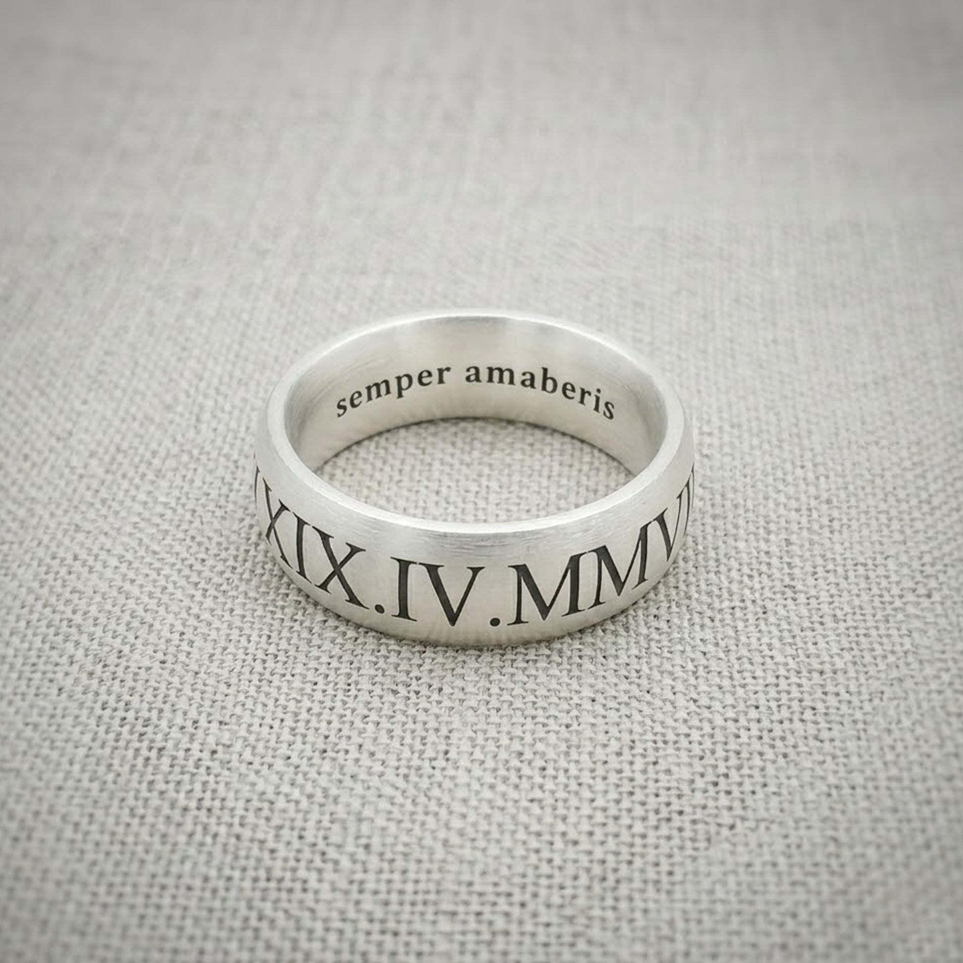 Silver ring with engraved text on a gray fabric background
