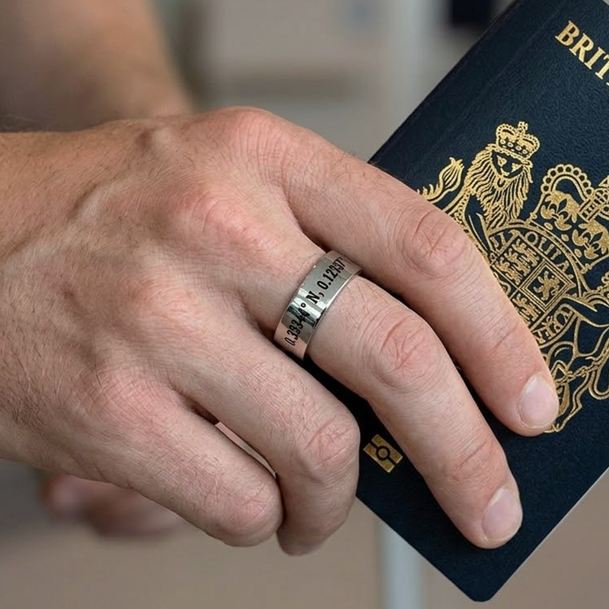 Hand wearing a ring with engraved text, holding a British passport.