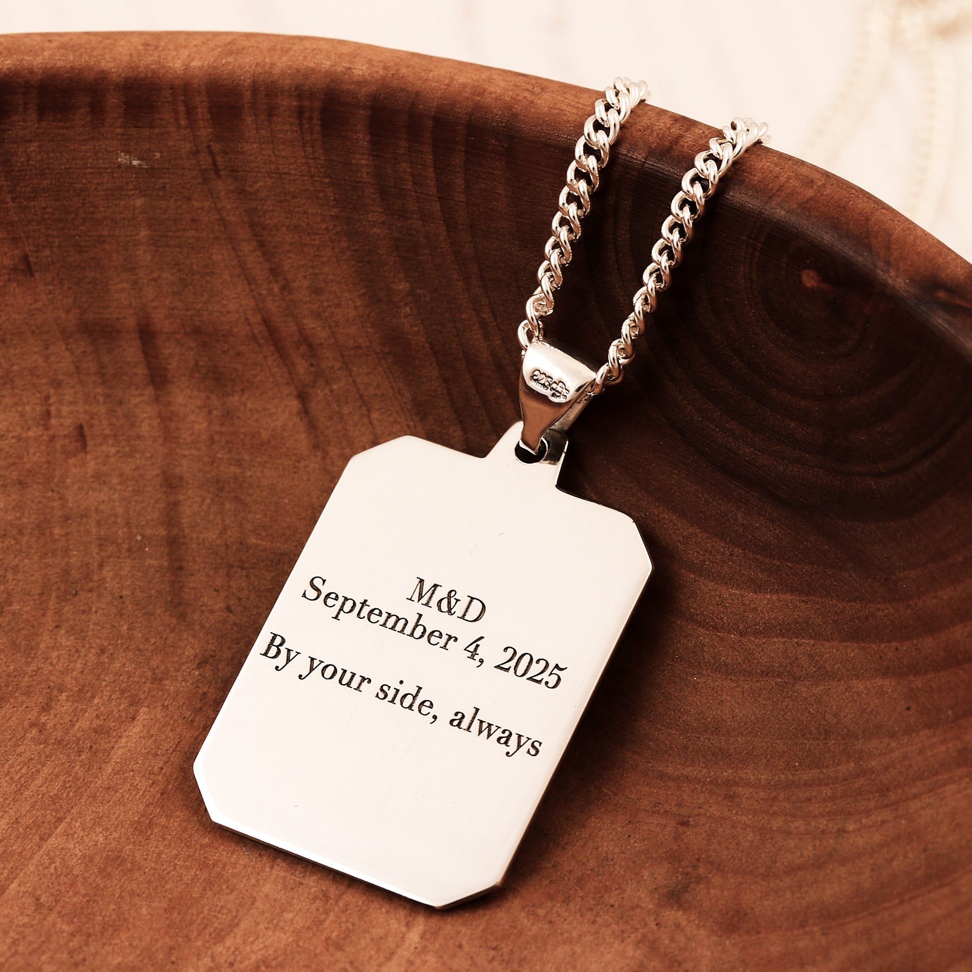 Silver dog tag necklace with engraved text on a wooden surface