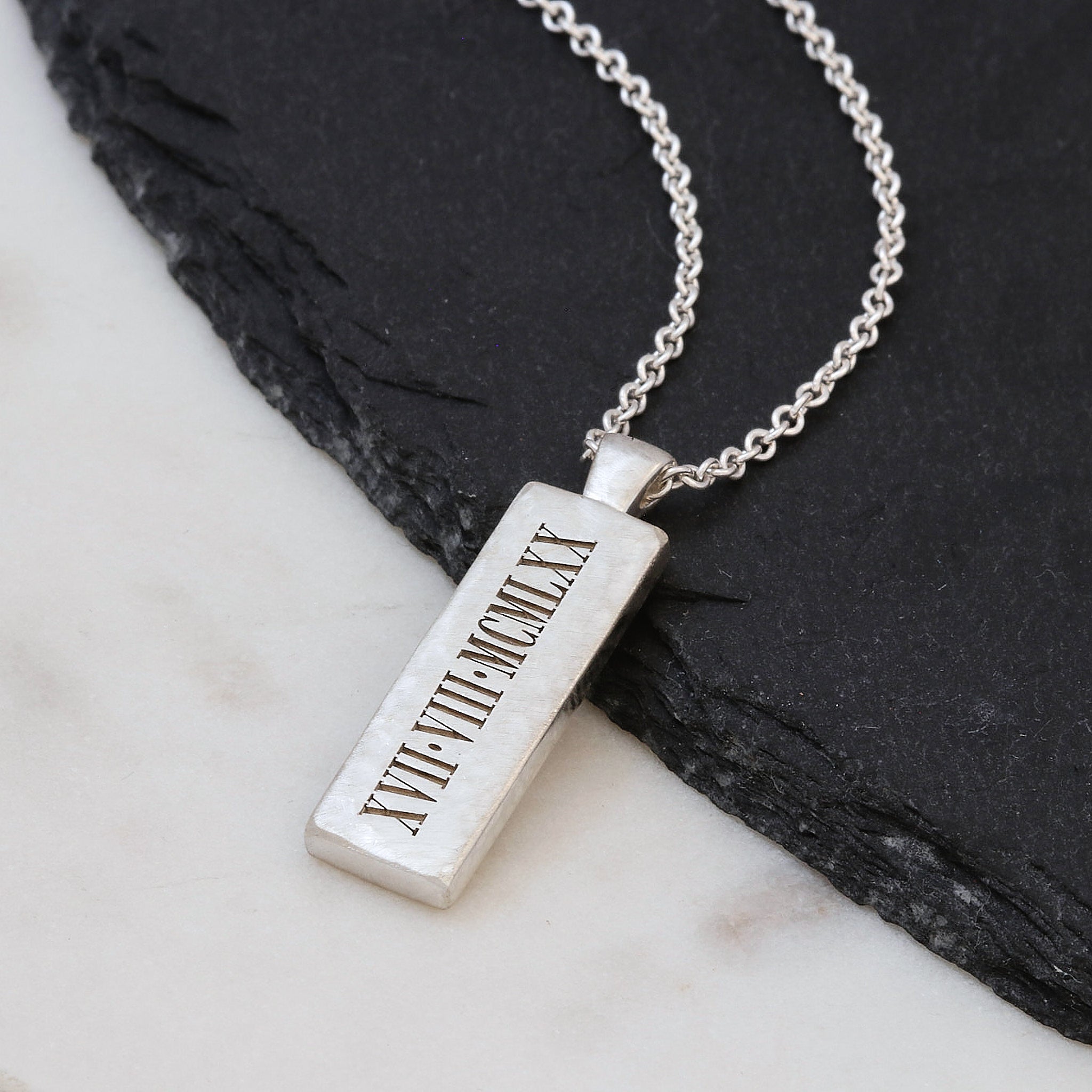 Silver necklace with a rectangular pendant on a marble surface