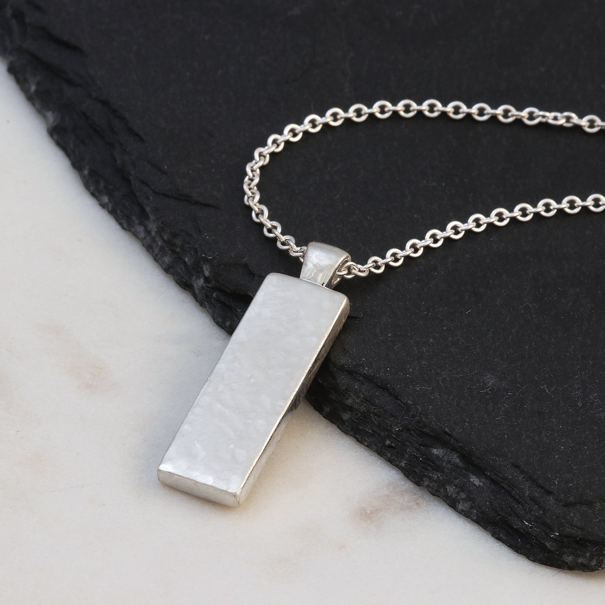 Silver necklace with a rectangular pendant on a dark stone surface