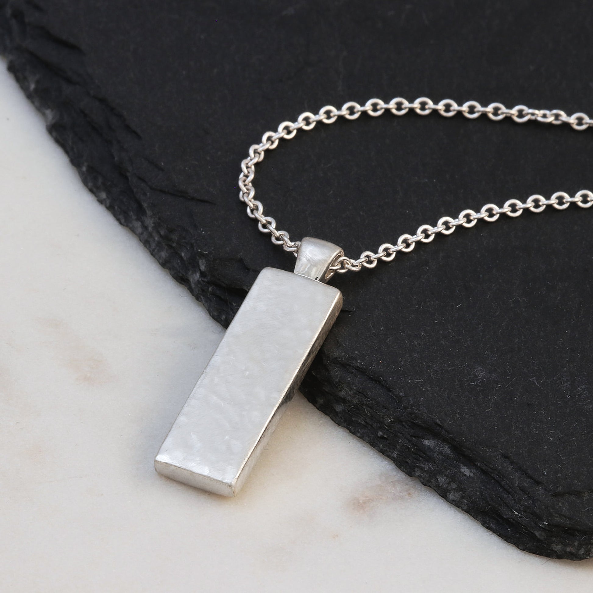 Silver necklace with a rectangular pendant on a dark stone surface