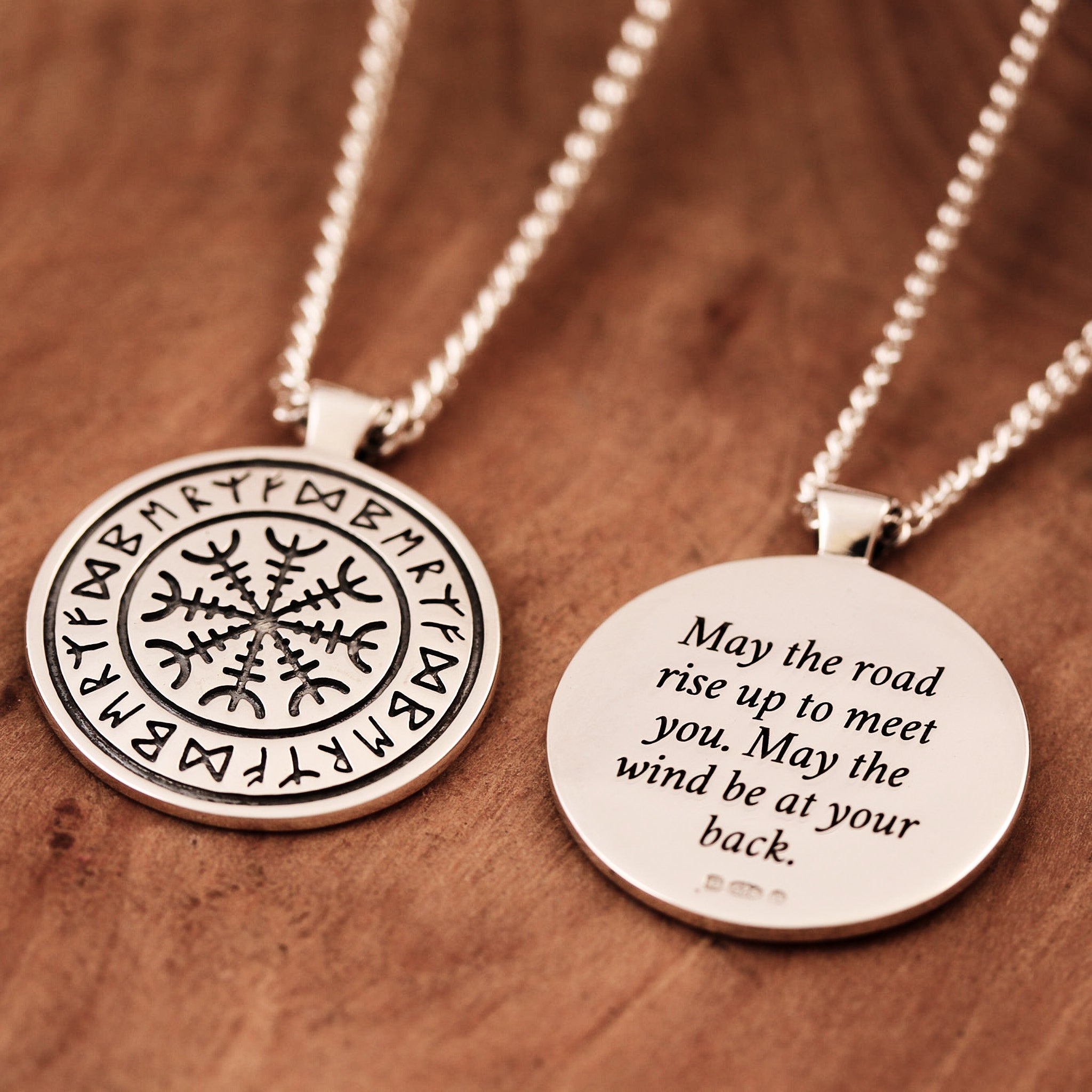 Two silver necklaces with engraved rune designs on a wooden surface