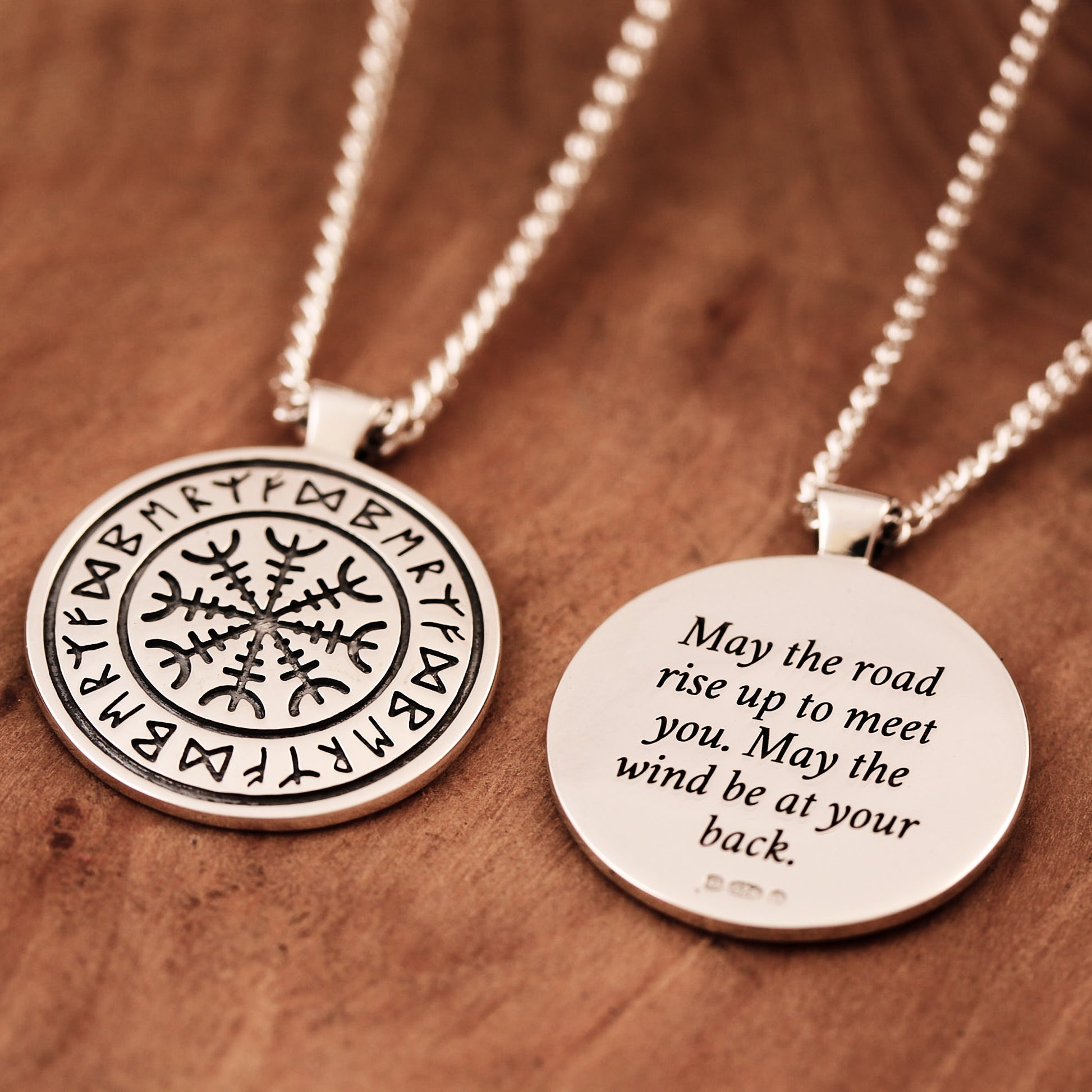 Two silver necklaces with engraved rune designs on a wooden surface