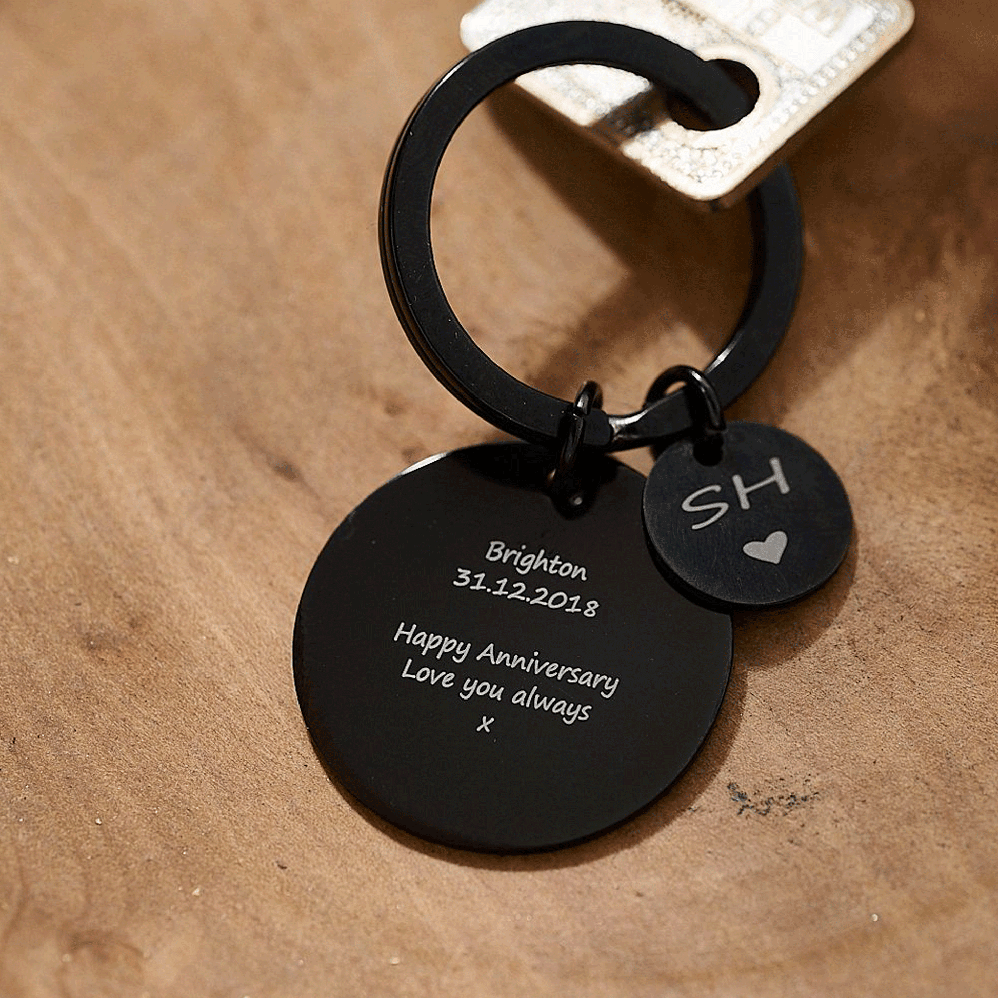 Black keychain with engraved message on a wooden surface