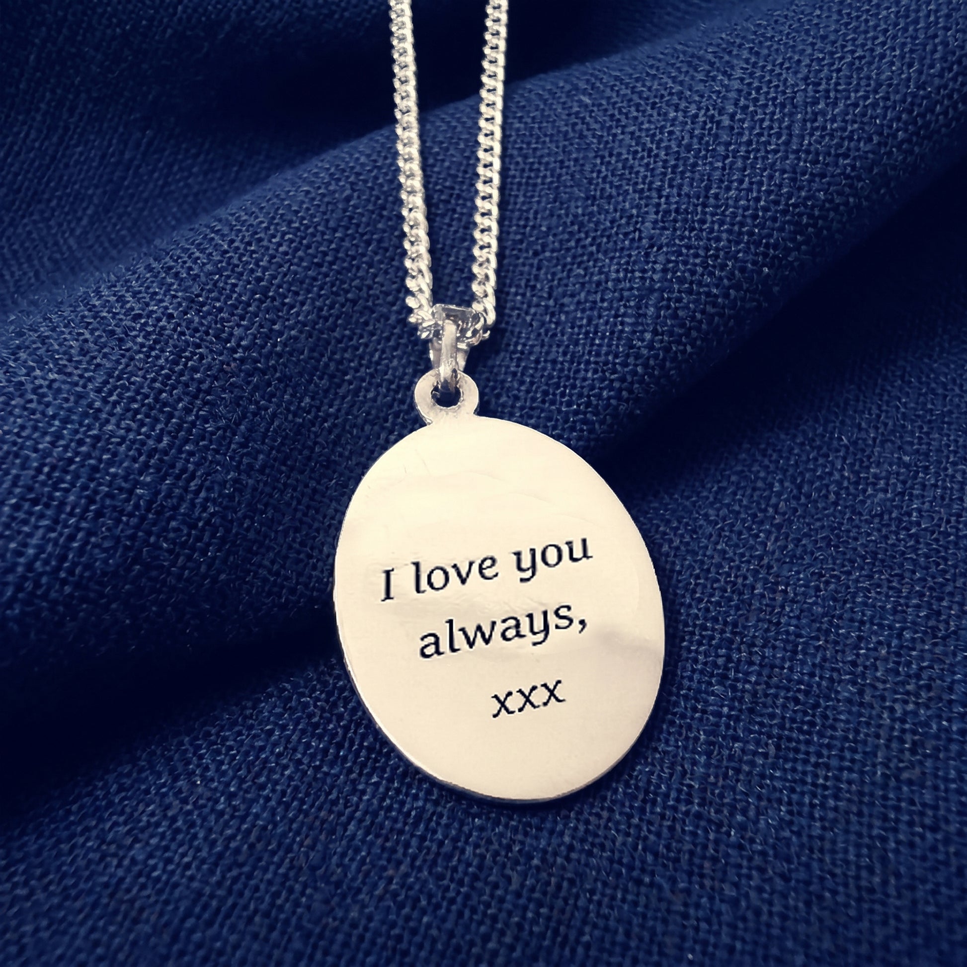 Silver necklace with a pendant that says 'I love you always, xxx' on a blue fabric background