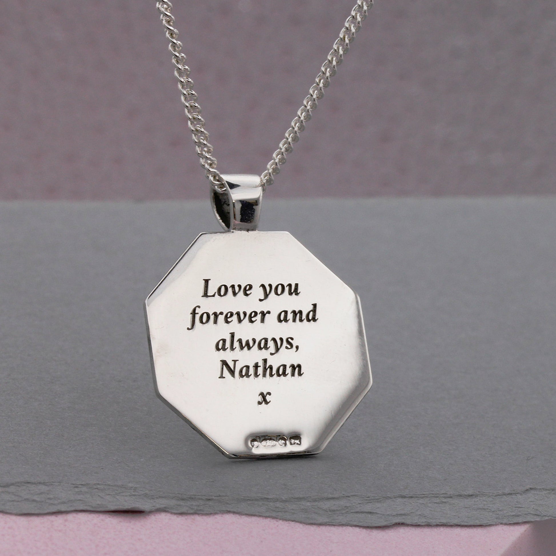 Silver necklace with an engraved pendant on a gray surface