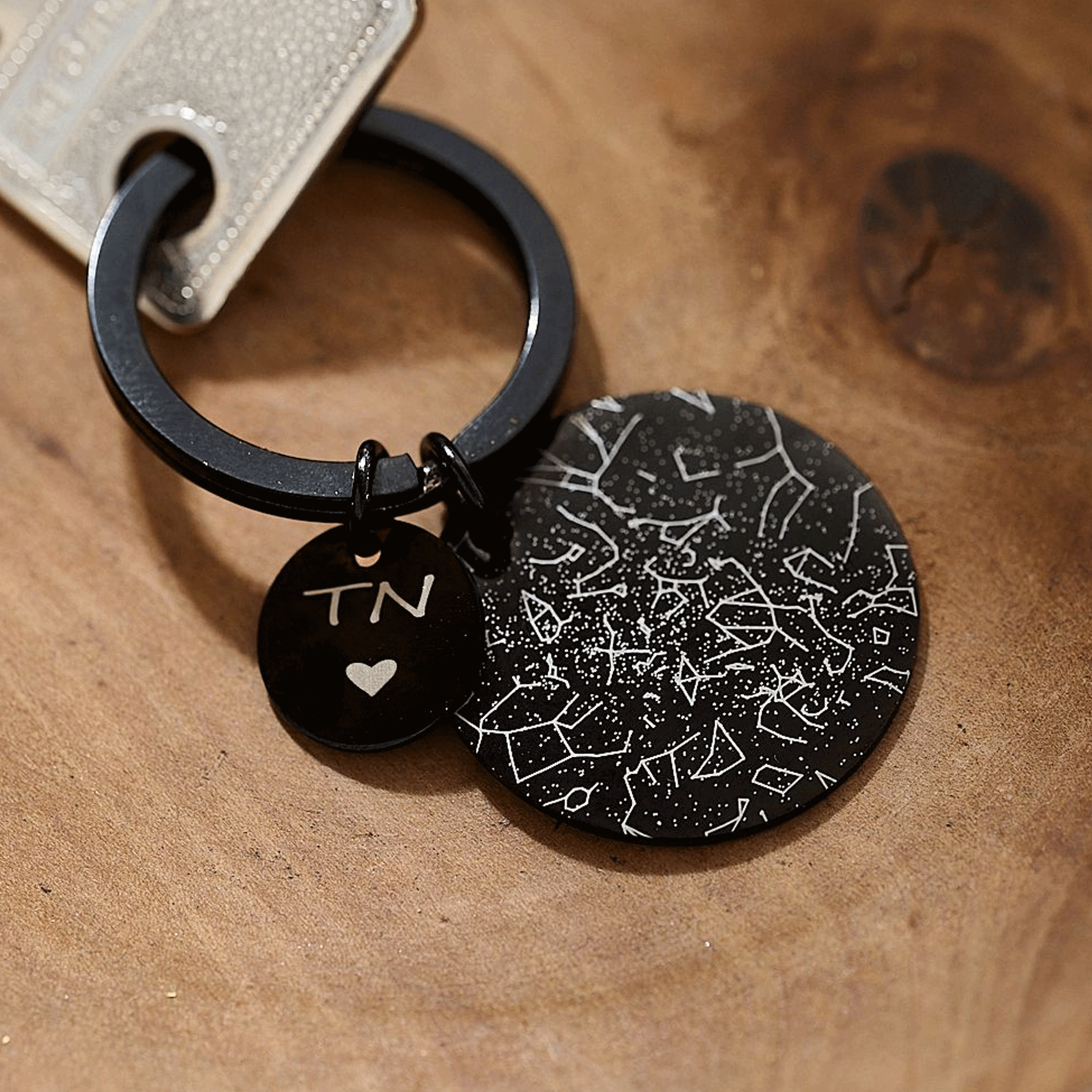 Black keychain with engraved star constellation design on a wooden surface