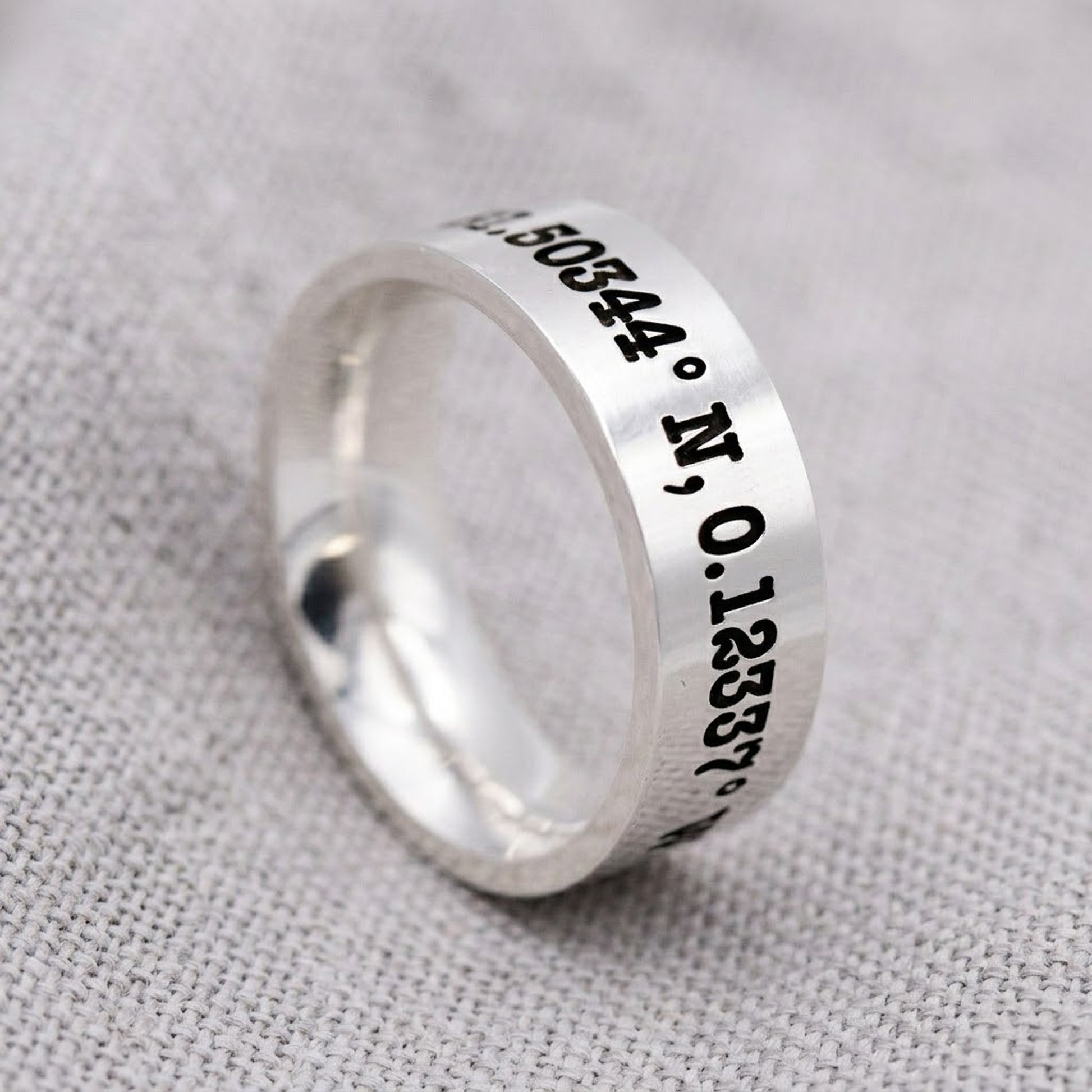 Silver ring with engraved coordinates on a gray fabric background