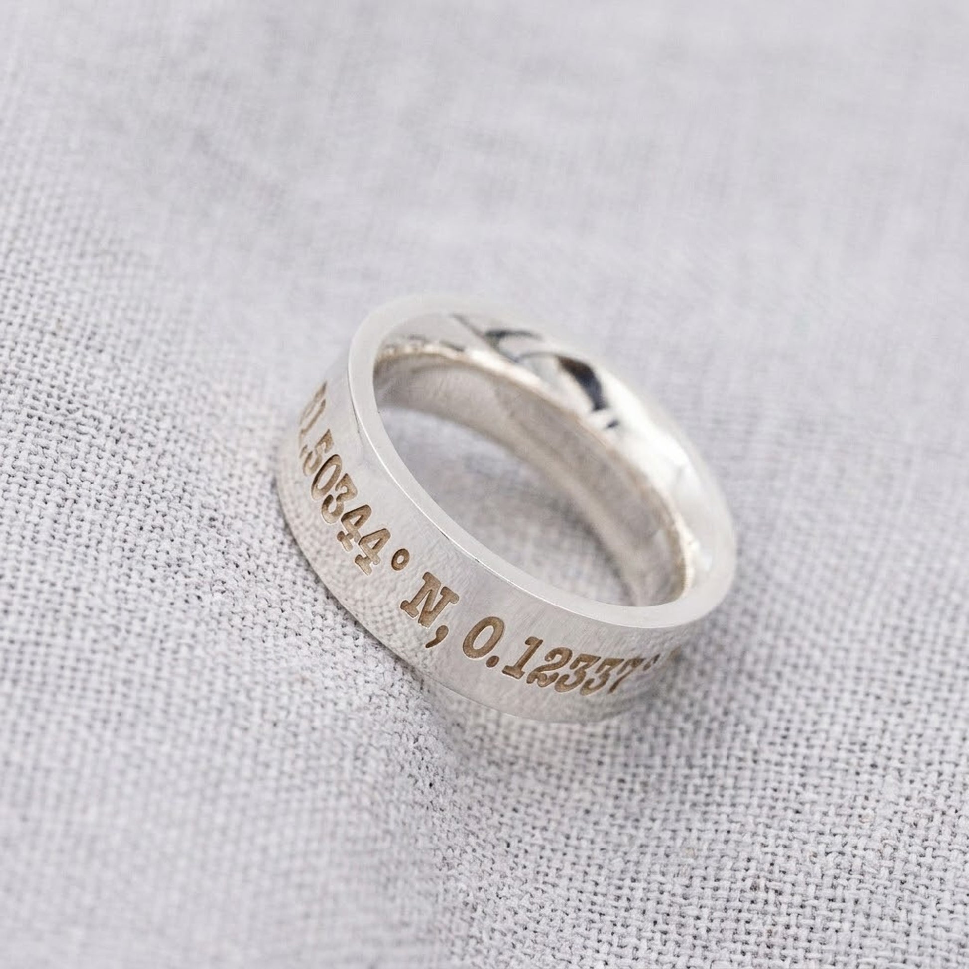 coordinates engraved silver ring on fabric background
