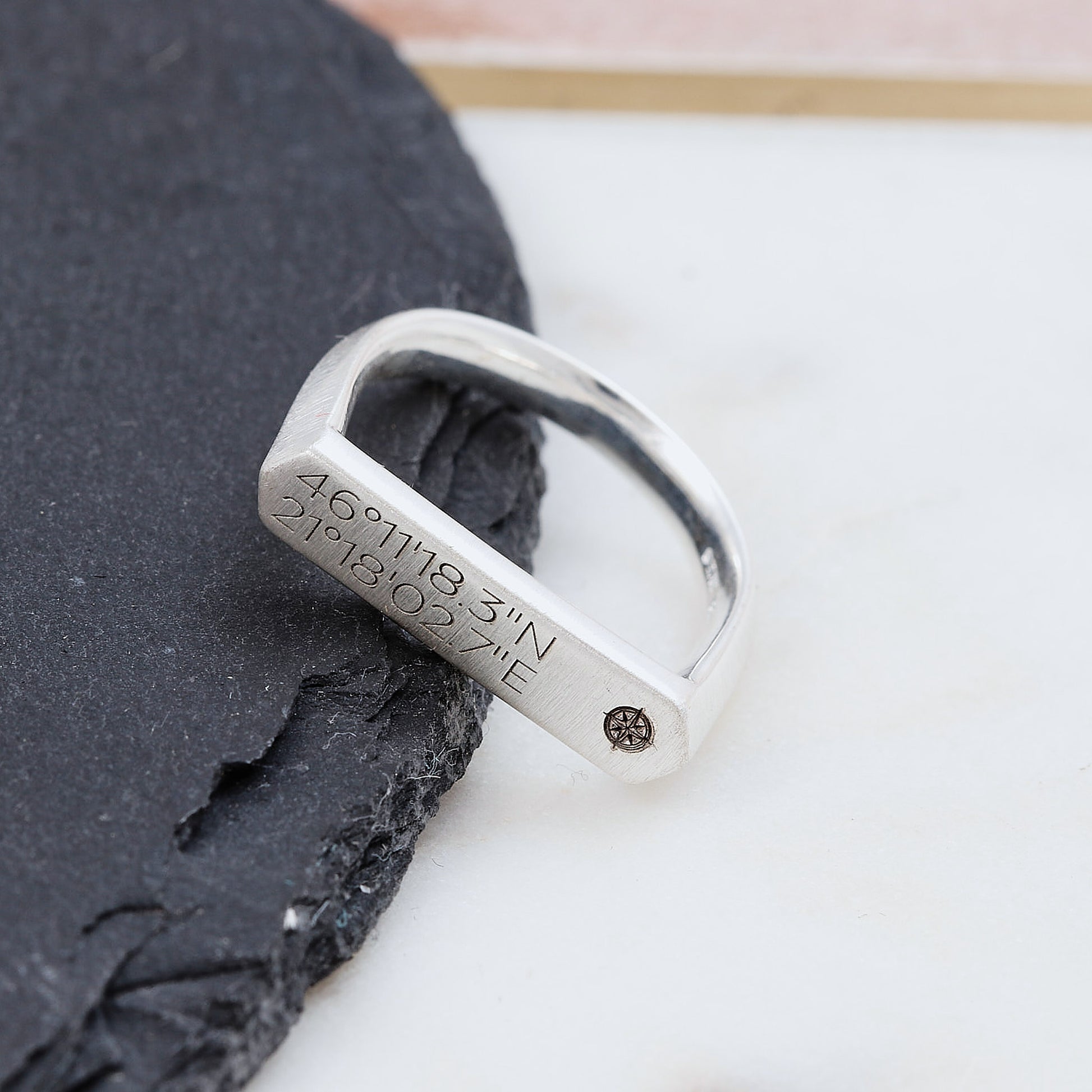 Silver matte finish signet ring with engraved coordinates on a dark stone surface
