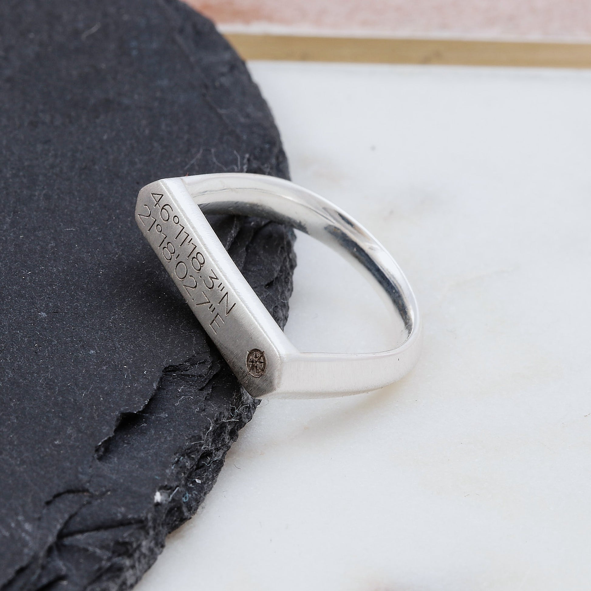 Silver matte finish signet ring with engraved coordinates on a dark stone surface