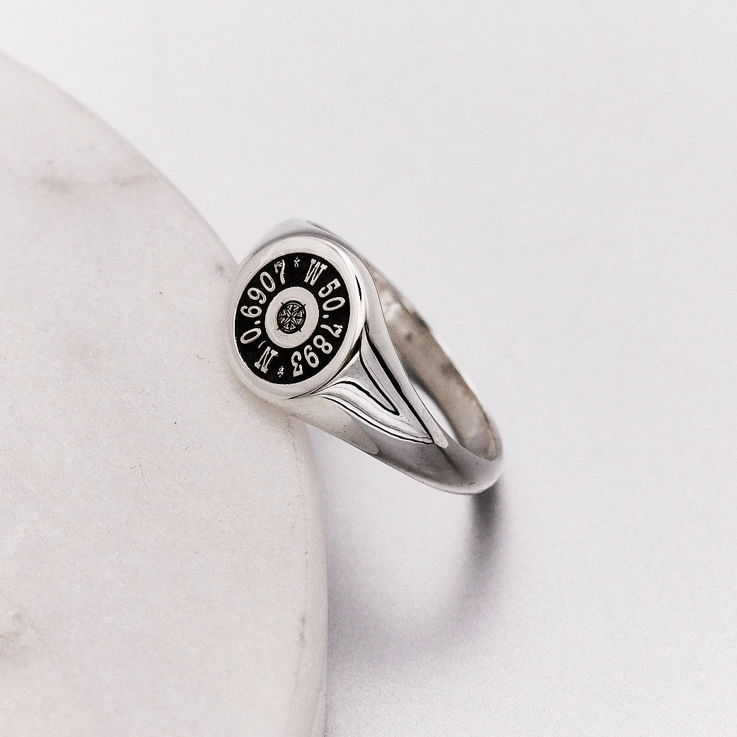 Silver ring with engraved coordinates on a light gray background