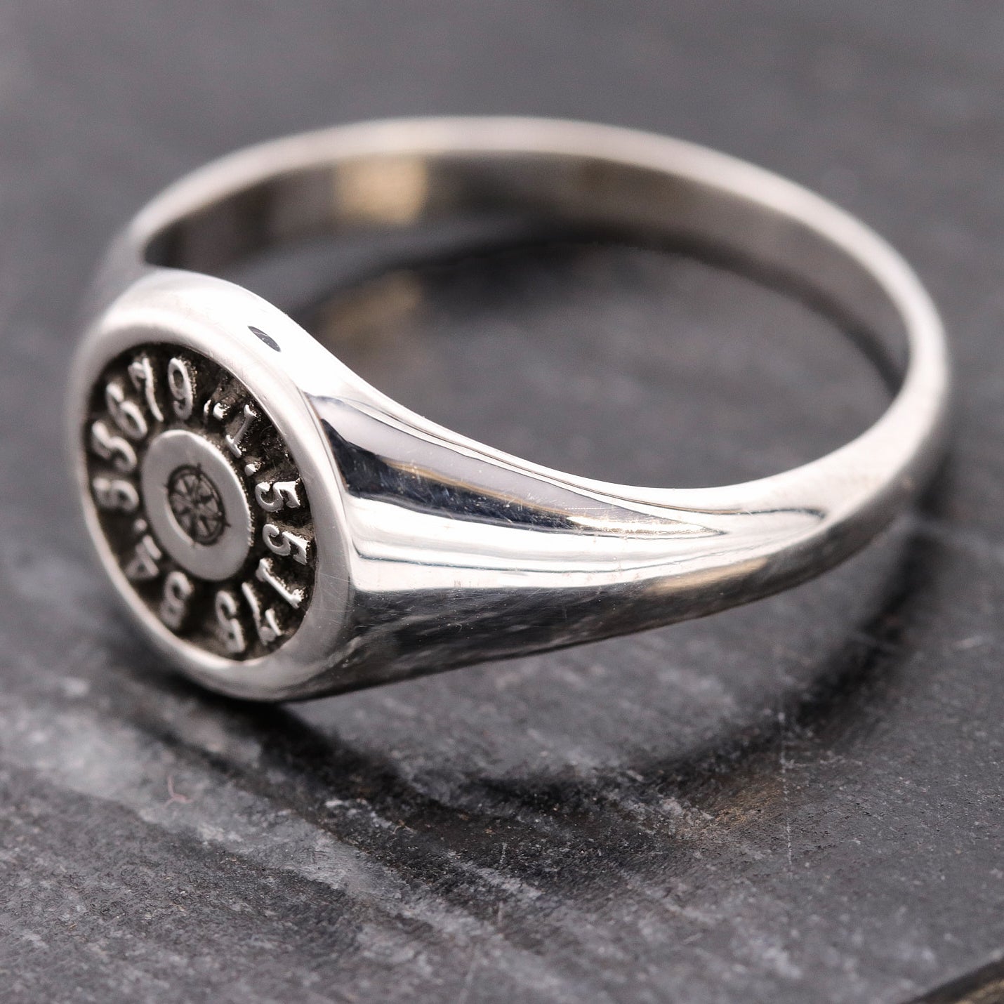 Silver ring with engraved coordinates on a dark stone surface