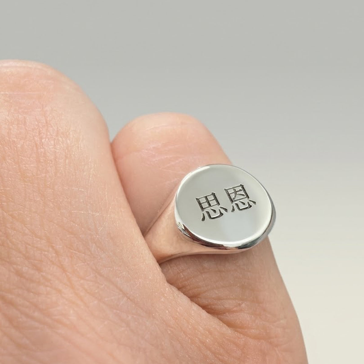 A silver signet ring with two engraved Chinese characters, shown worn on a person's finger against a neutral gray background.