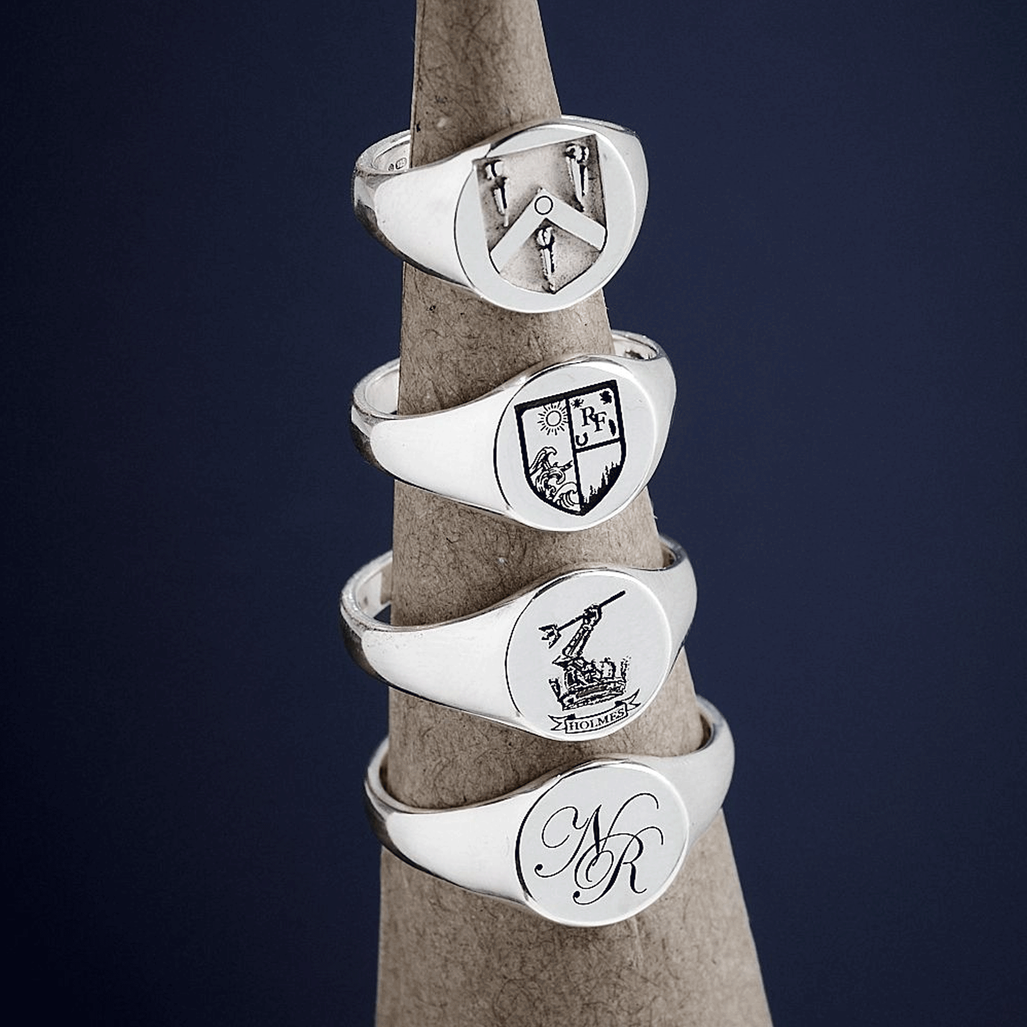 Set of silver signet rings with engraved designs on a wooden stick against a dark background