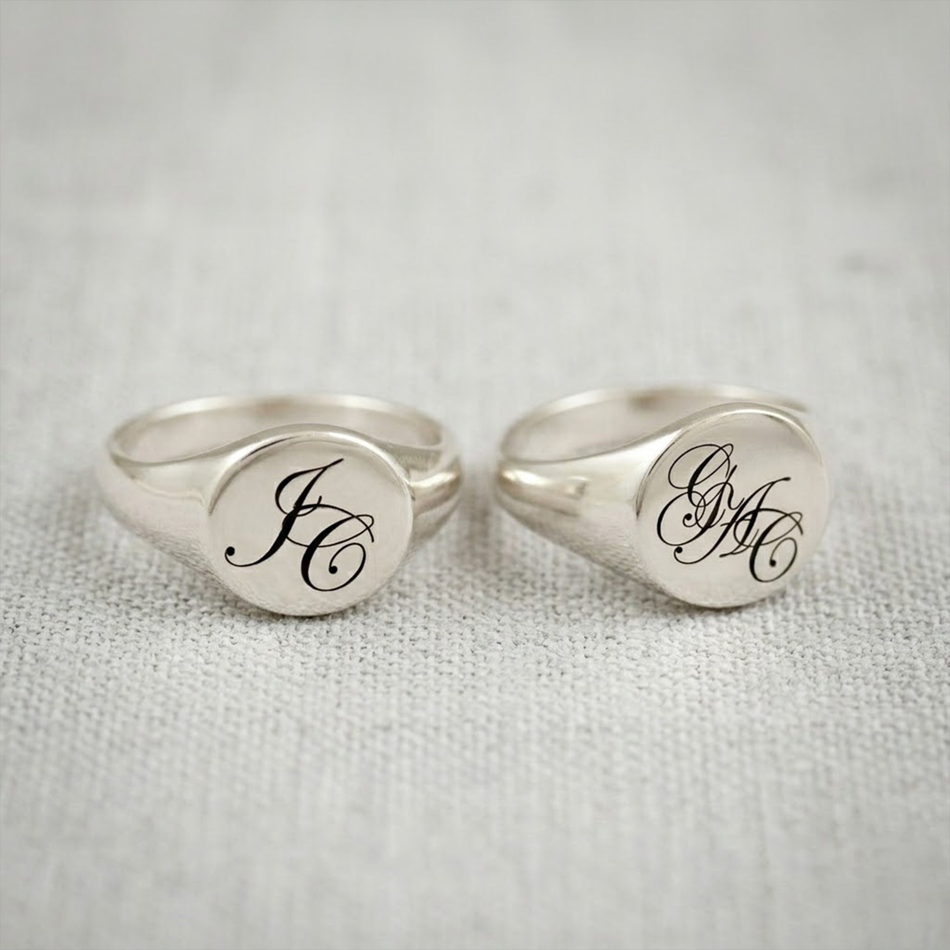 Two silver rings with engraved initials on a textured gray background