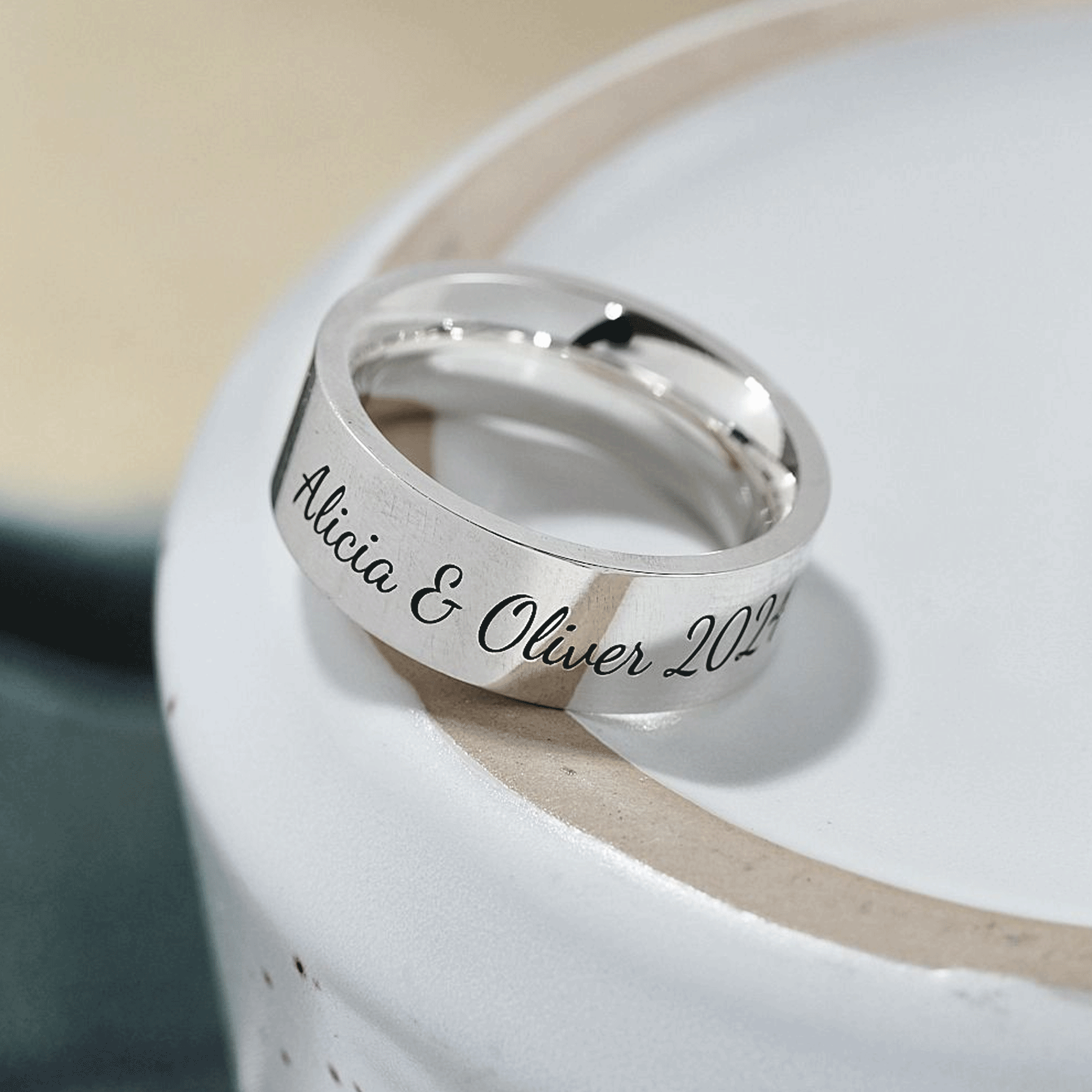 Silver ring with engraved names and date on a white surface
