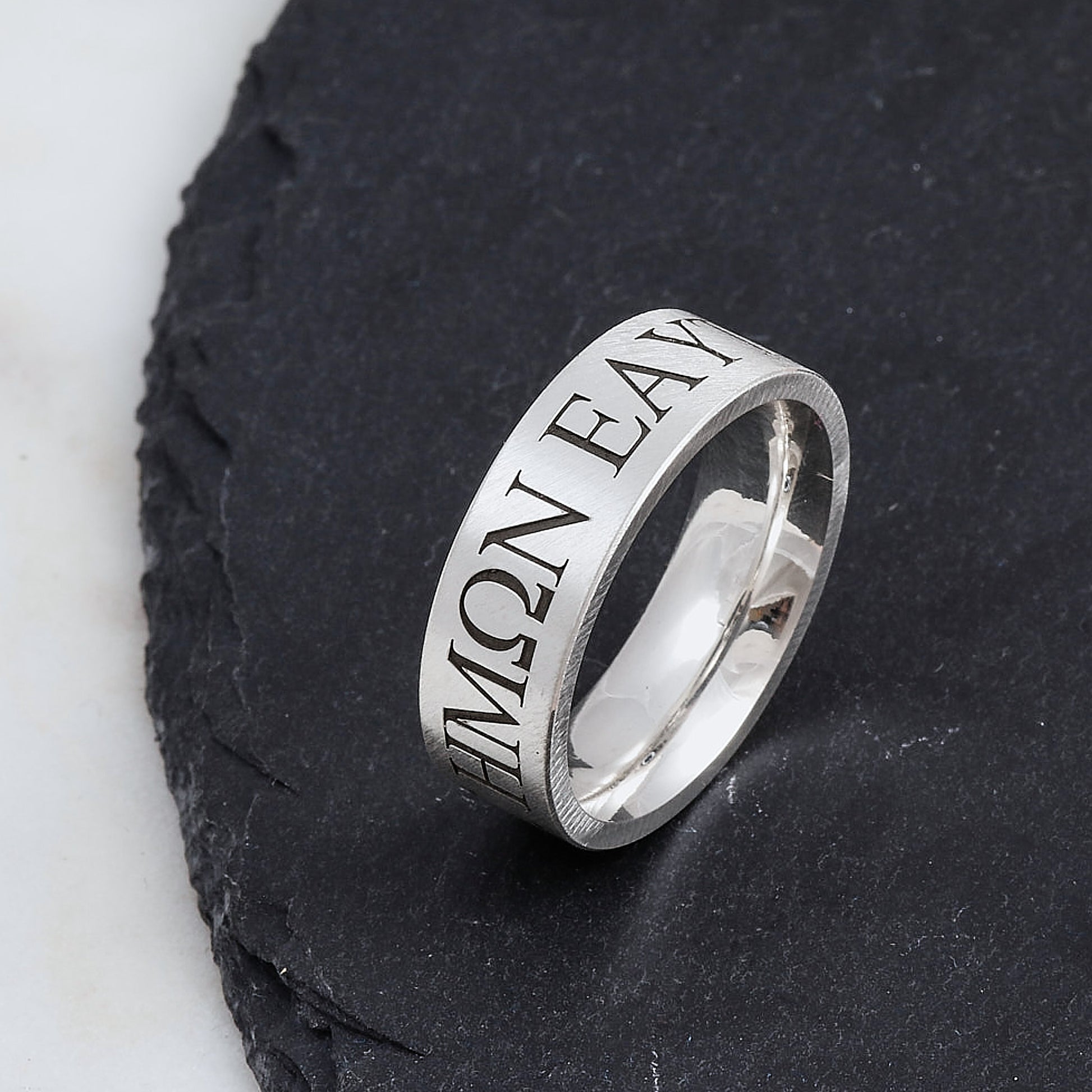 Silver ring with engraved greek text in serif font on a dark stone surface