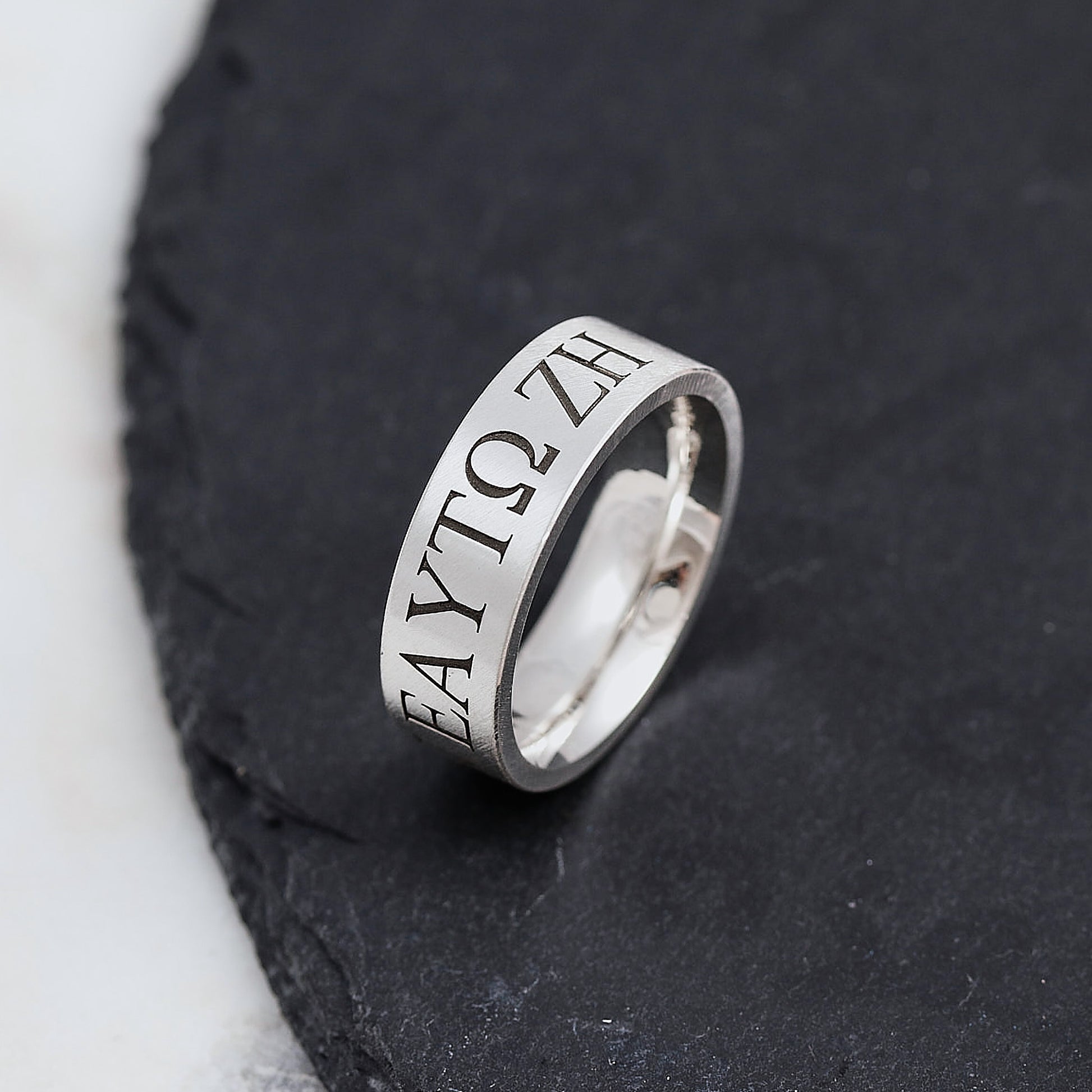 Silver ring with engraved greek text in serif font on a dark stone surface