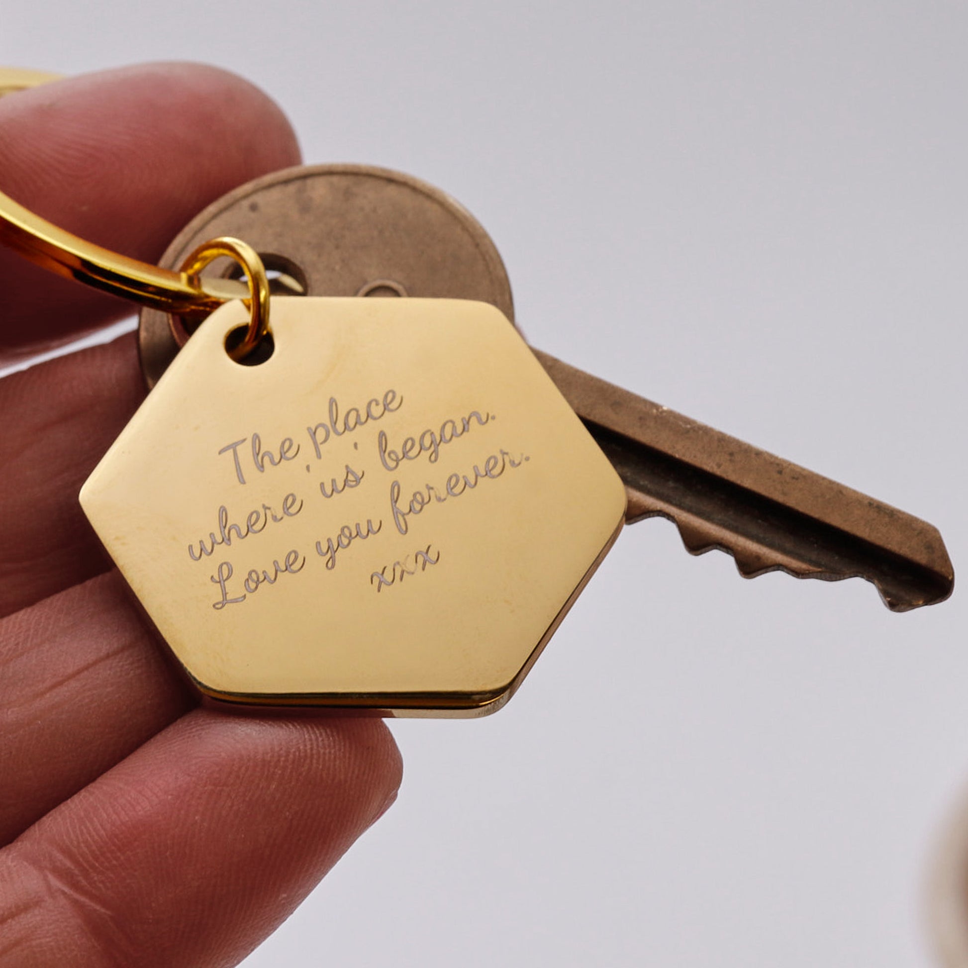 Gold keychain with engraved message held by a hand against a neutral background