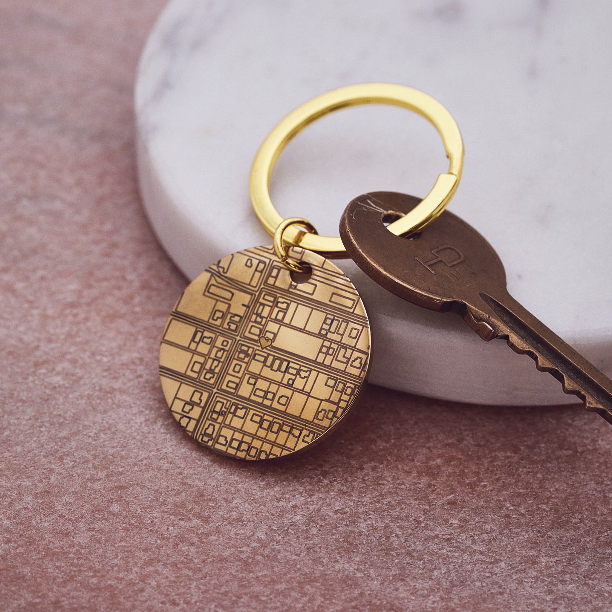 Gold keychain with geometric pattern and bronze key on a textured surface
