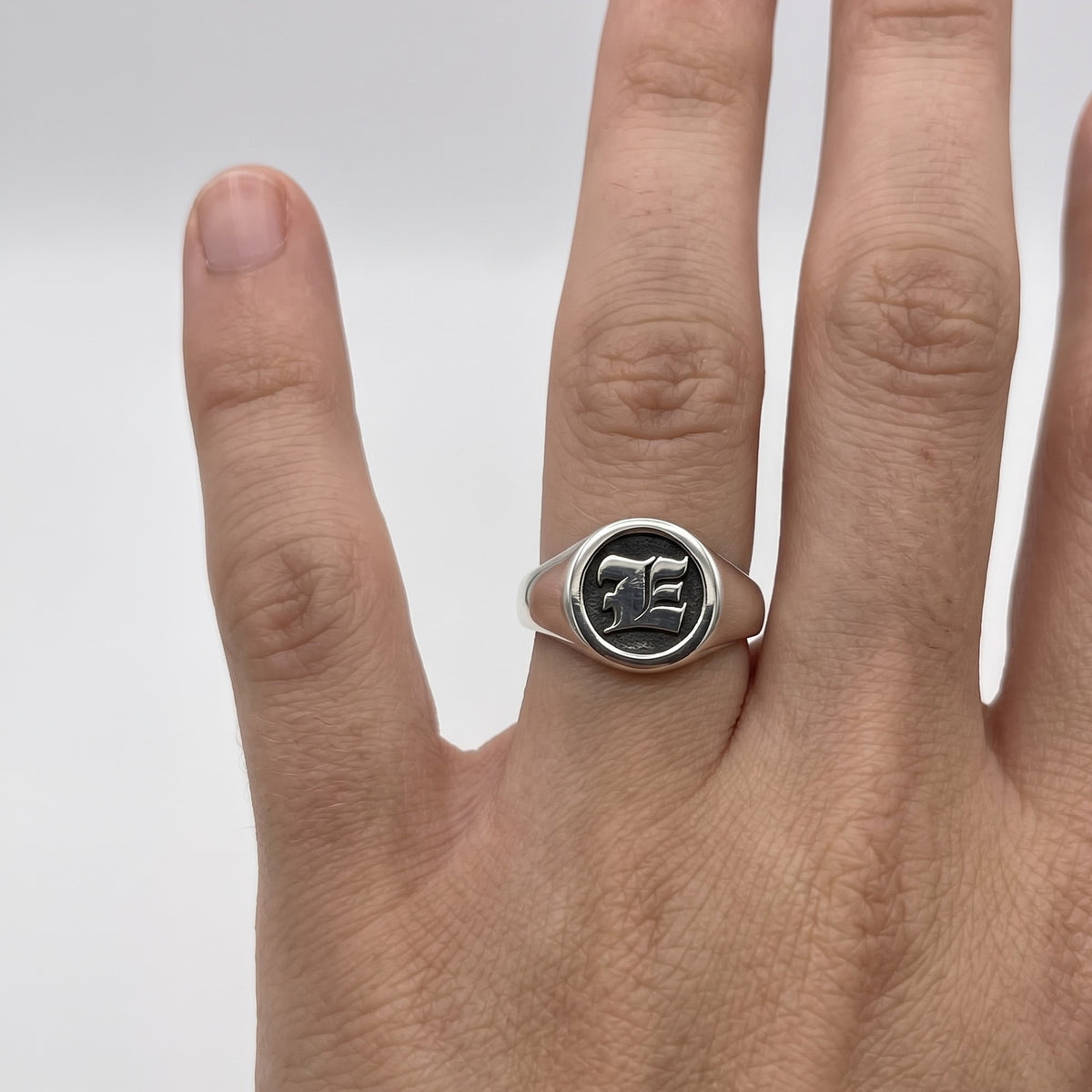 Silver signet ring with E engraved and oxidised detail on a persons hands