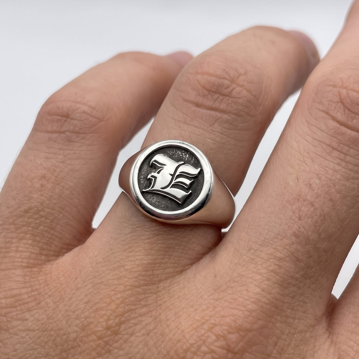 Gothic style engraved signet ring with E engraved on a persons hand