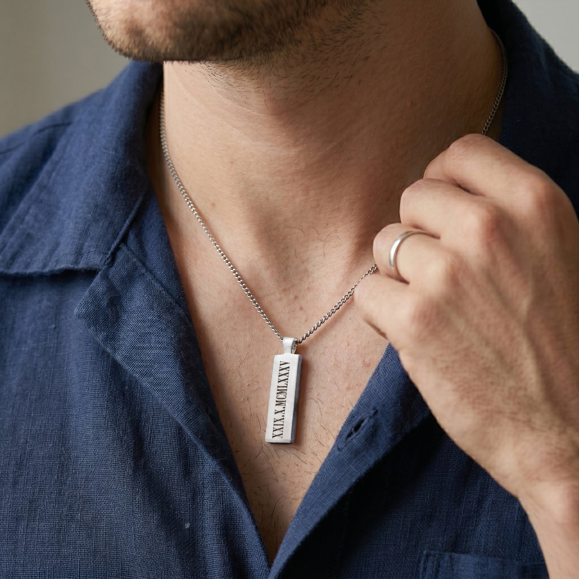 Man wearing a silver necklace with a pendant, adjusting it with his hand.