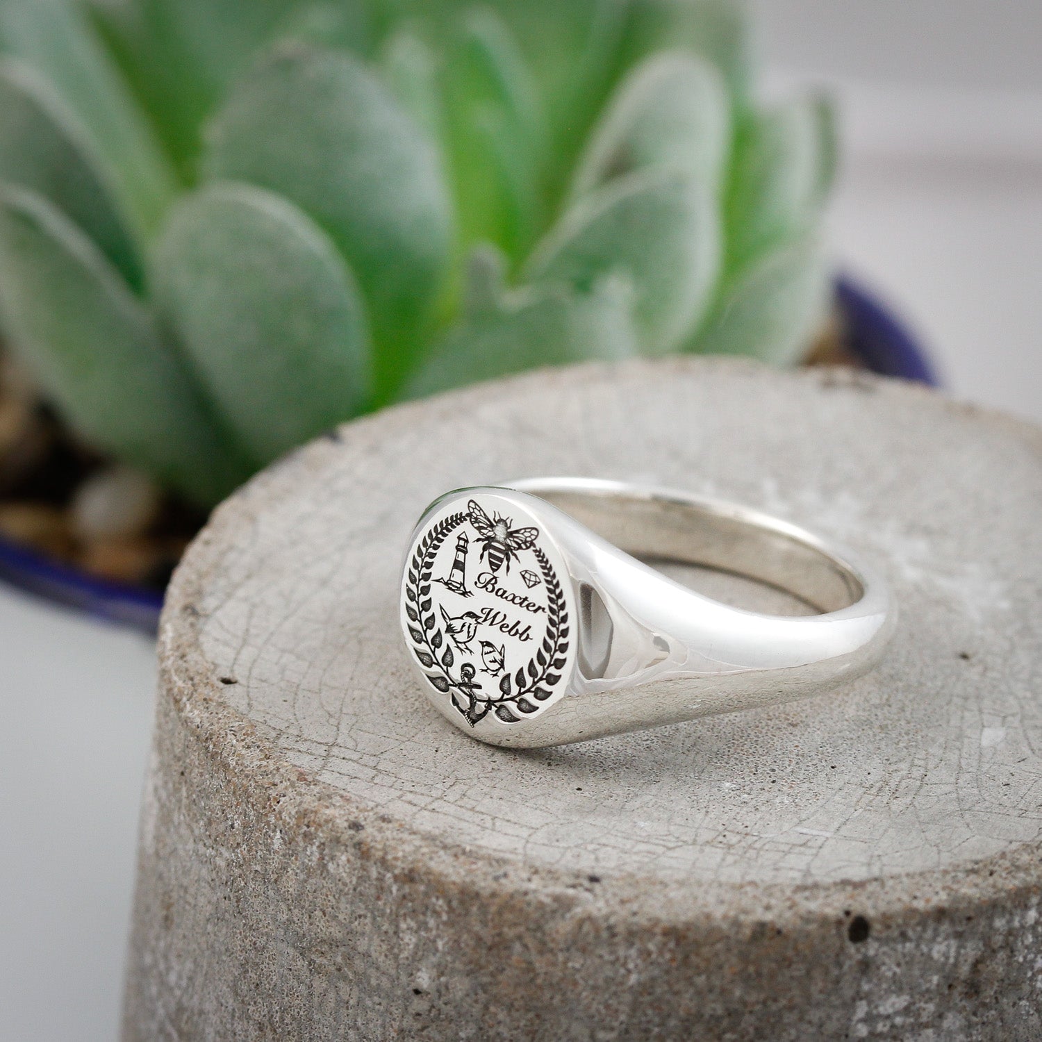 Silver ring with engraved design on a concrete surface with a plant in the background