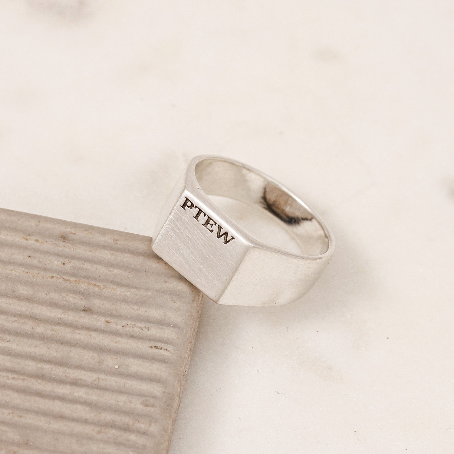 Silver signet ring with 'PIEW' engraving on a textured beige surface