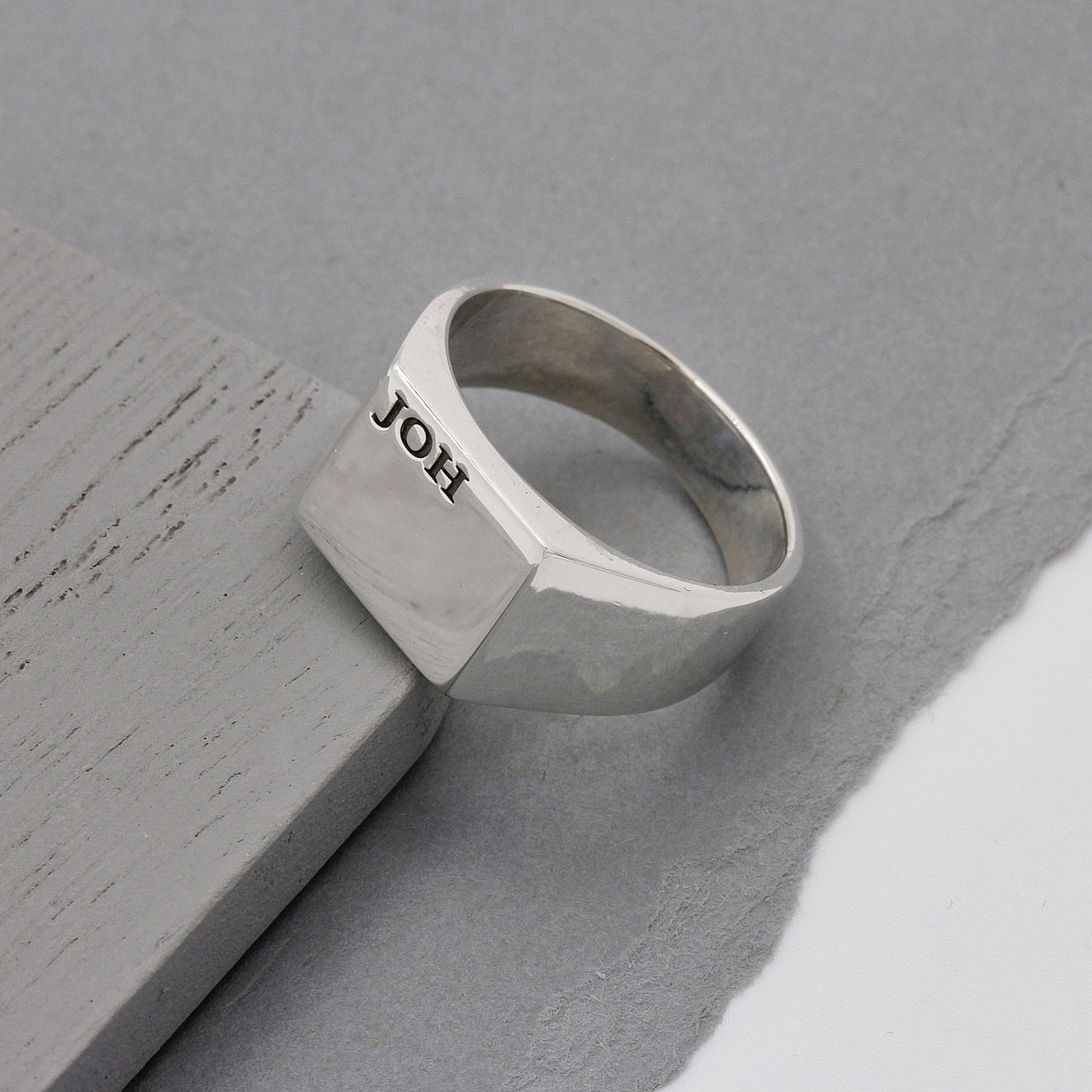 Silver ring with 'JOH' engraving on a gray surface