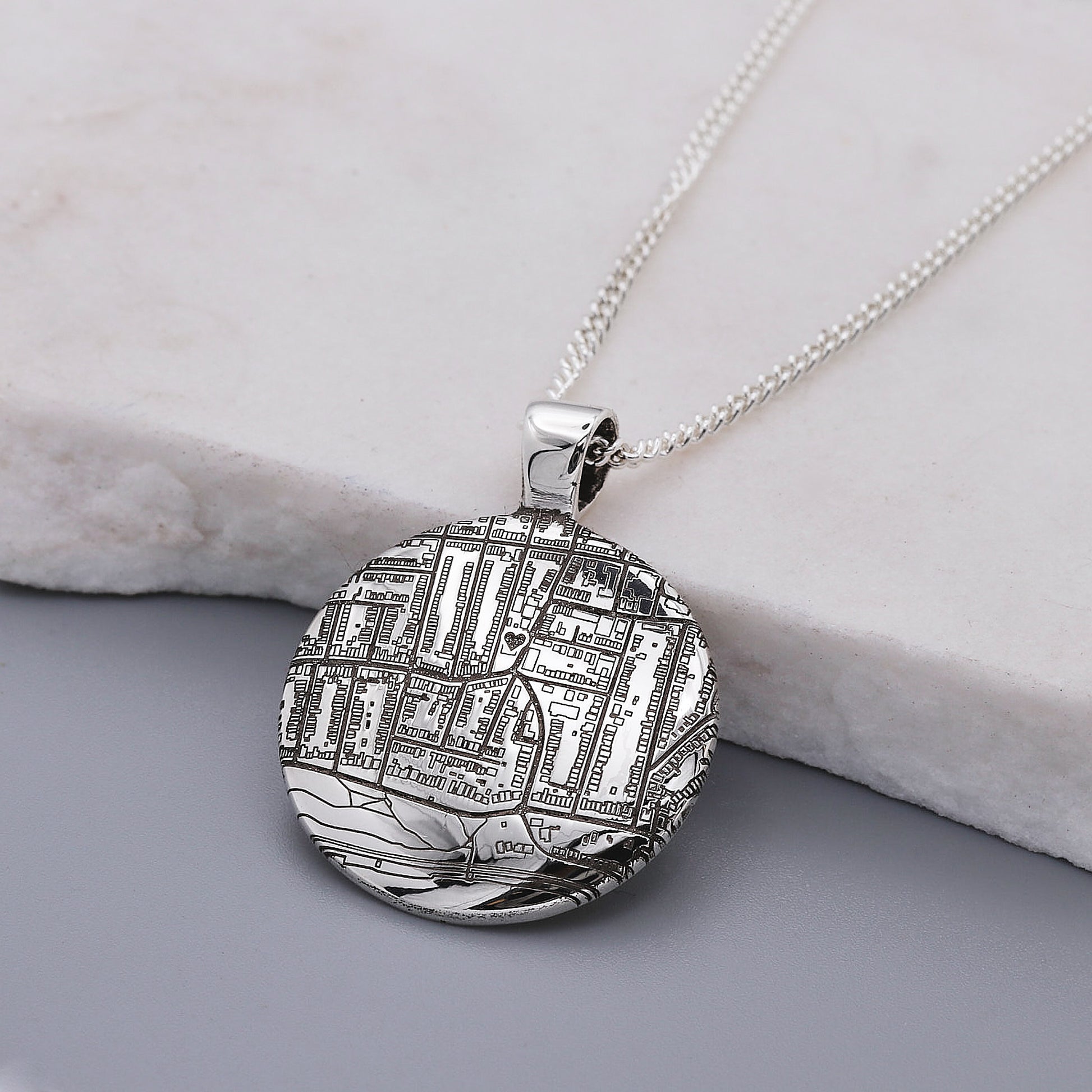 Silver map pendant with engraved design on a chain against a neutral background