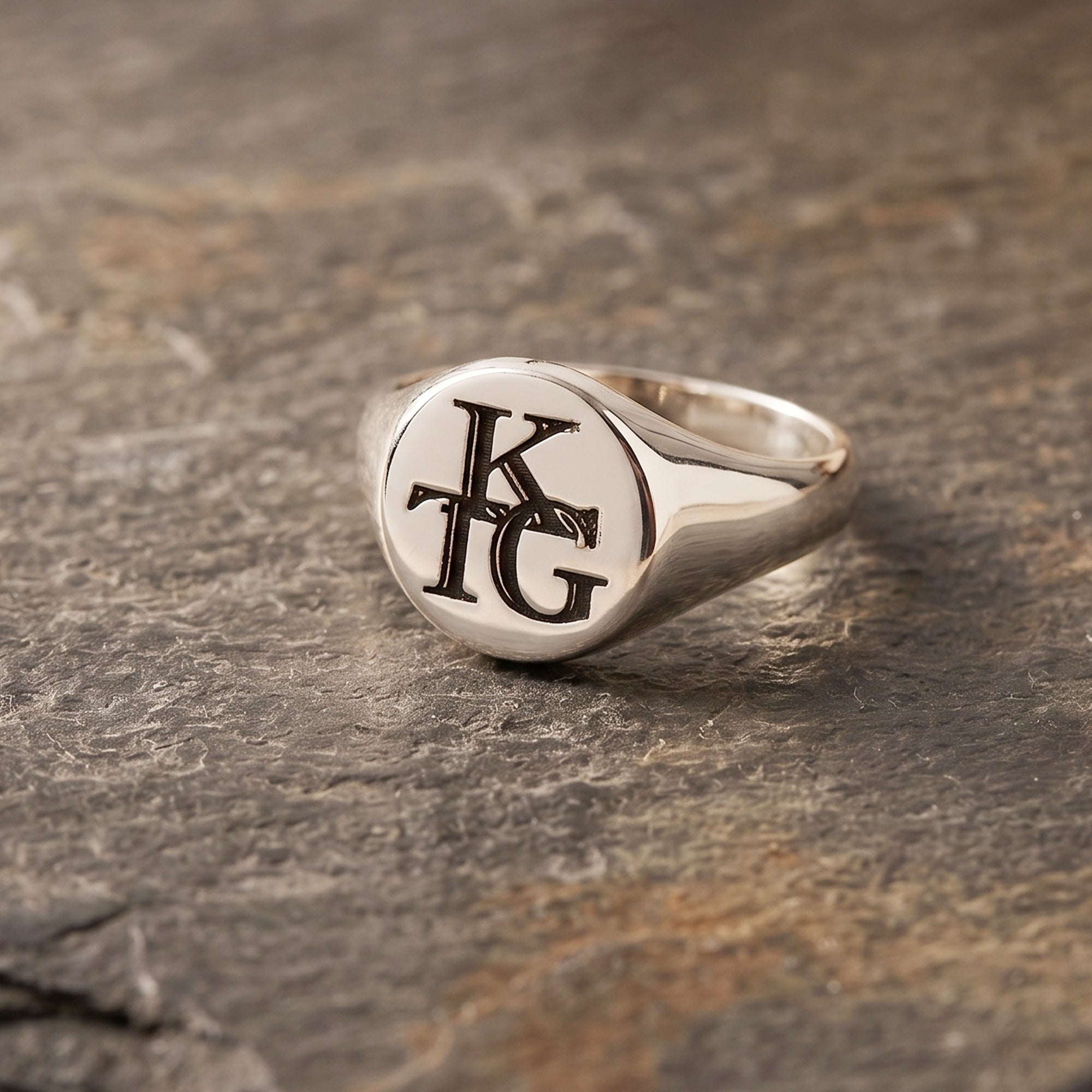 Silver ring with 'KG' initials on a stone surface
