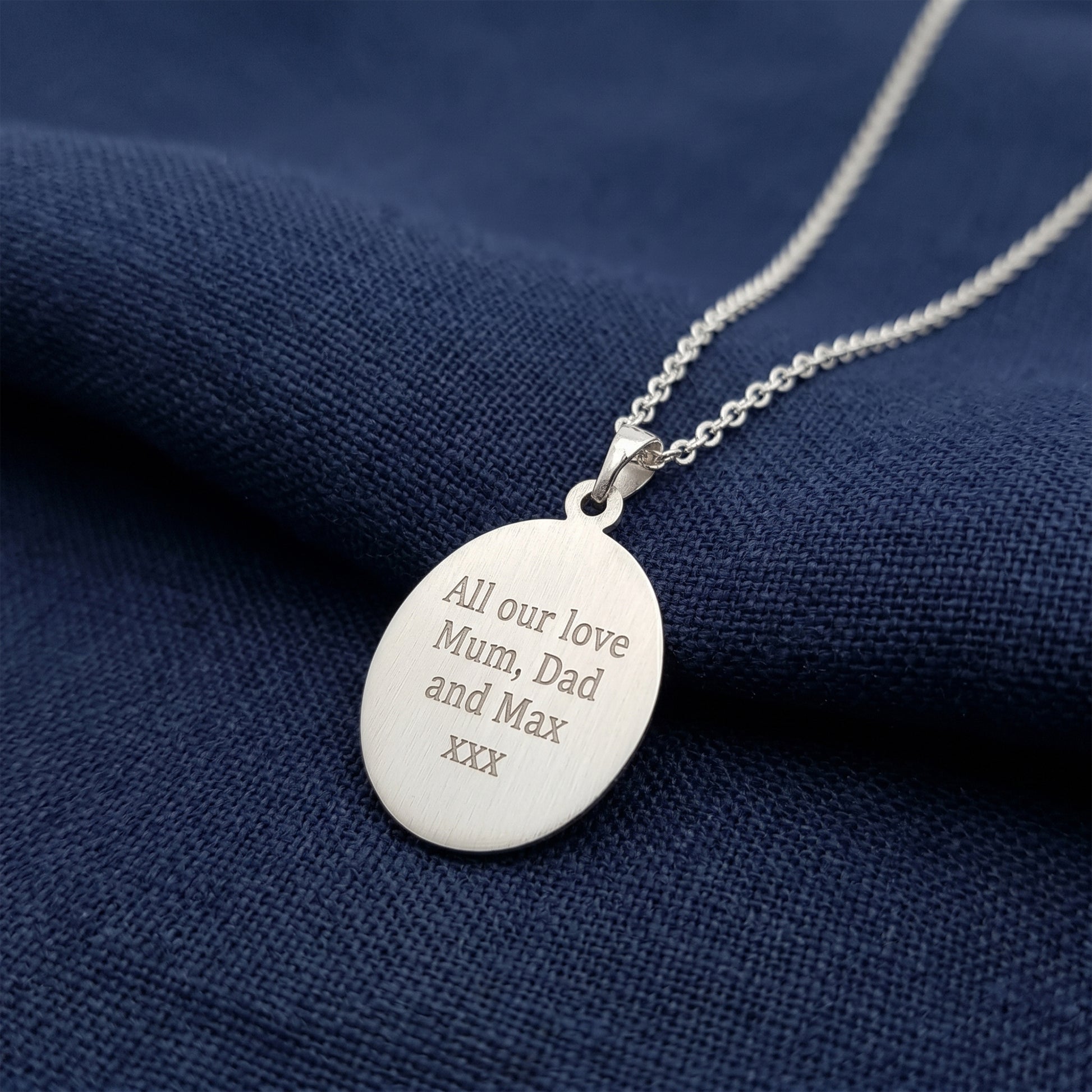 Silver necklace with an engraved pendant on a blue fabric background