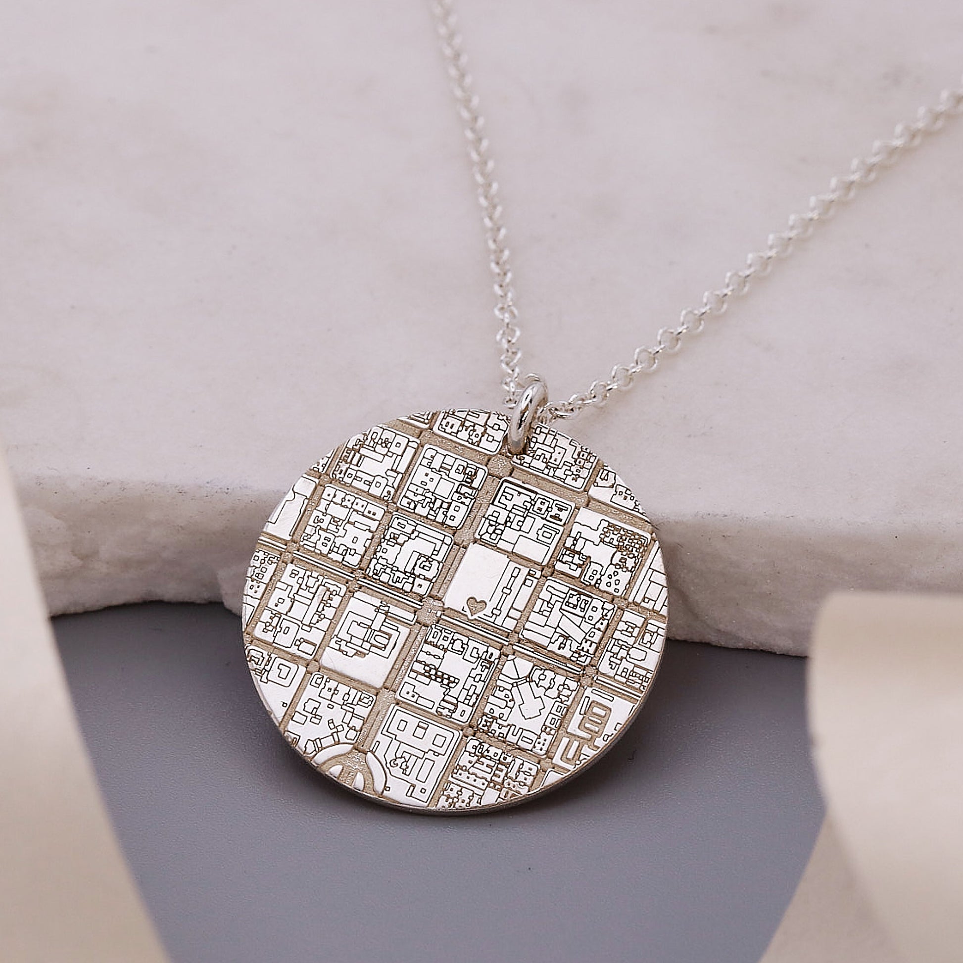 Silver necklace with a detailed map pendant on a soft surface