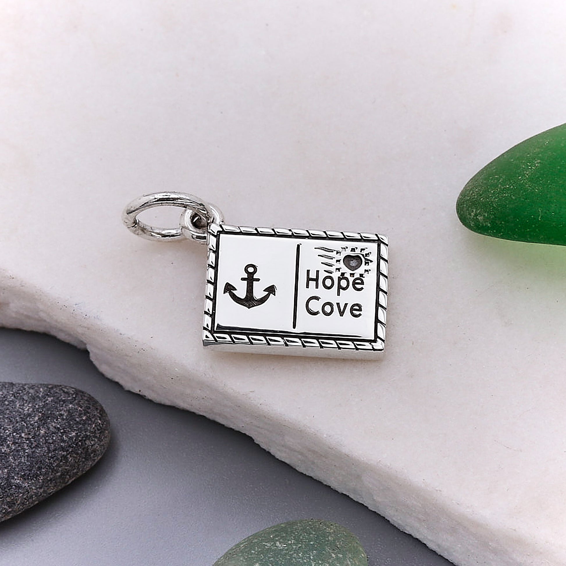 Silver postcard charm with 'Hope Cove' design on a white stone background