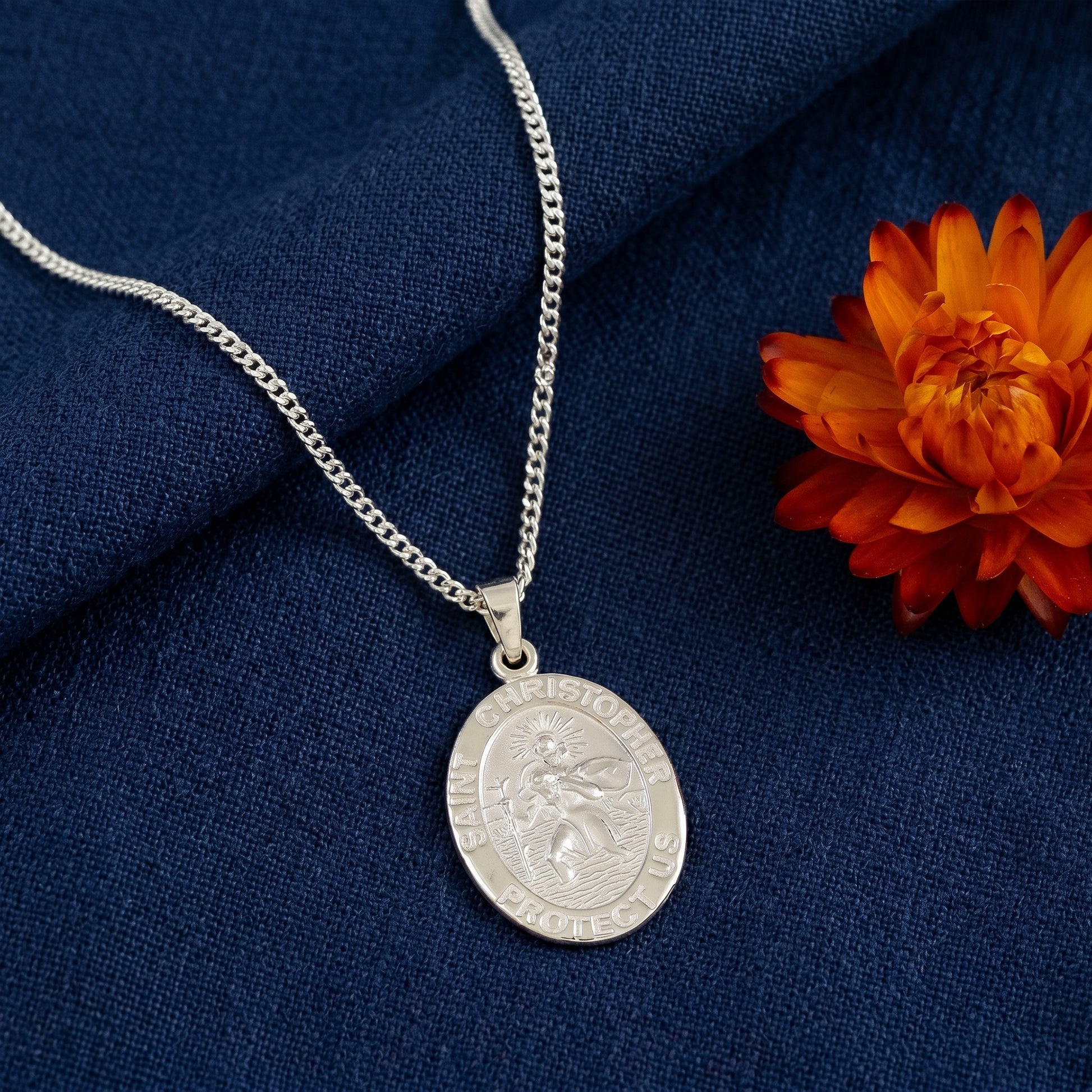Silver necklace with a round pendant on a blue fabric background with an orange flower.